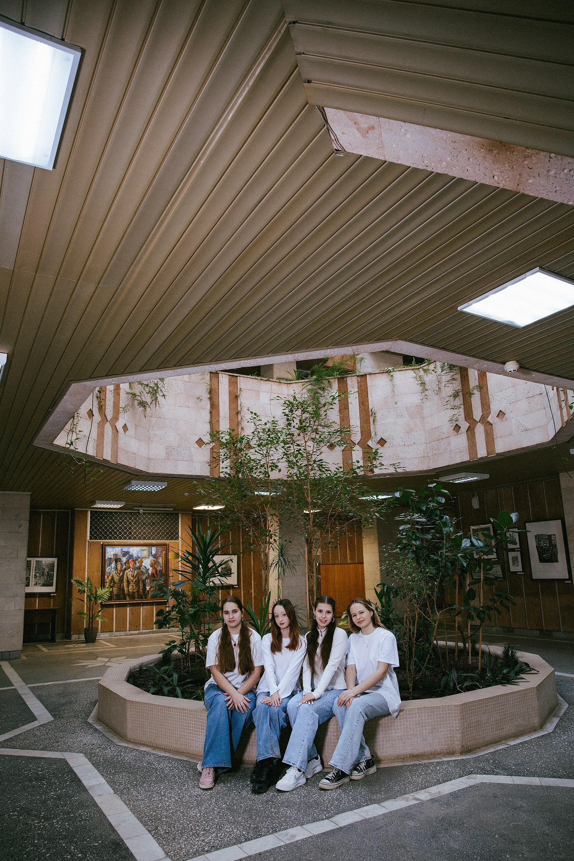 Группа выпускниц сидит в холле Дома профсоюзов, советский интерьер и растения, фотосессия для школьного альбома.