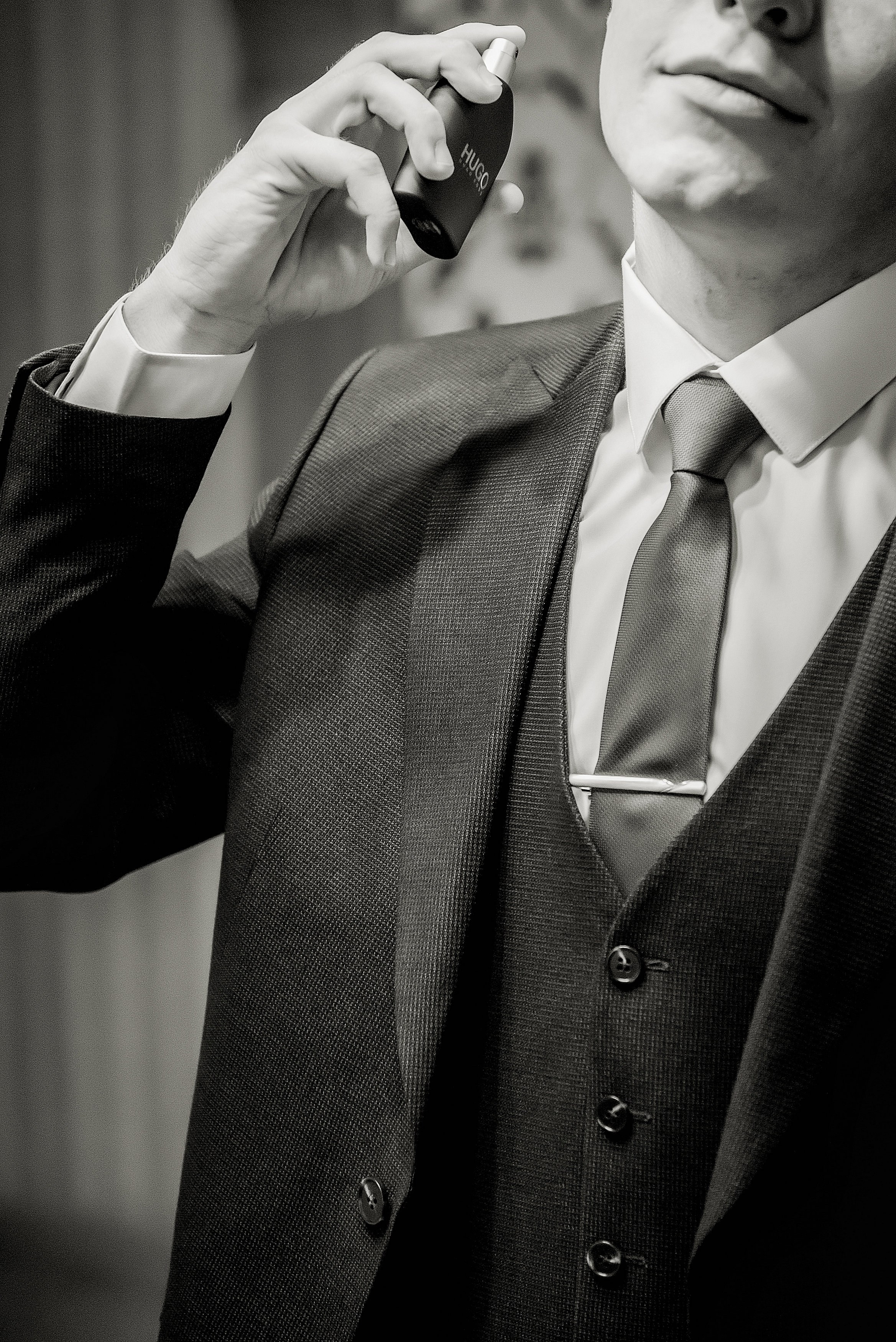 Чёрно-белая фотография мужчины в костюме и галстуке, который распыляет парфюм флакона бренда "Hugo".
