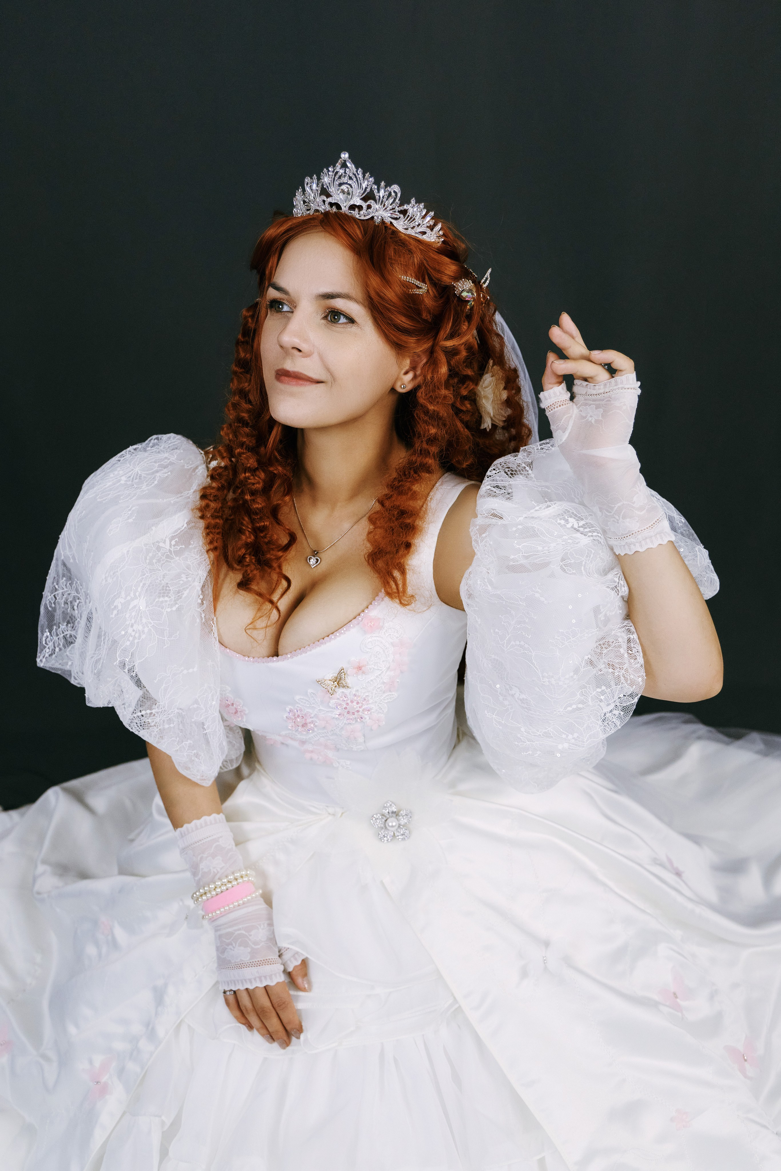 Красивая рыжеволосая девушка в белом платье позирует с короной на голове на тёмно-сером фоне, фото сверху