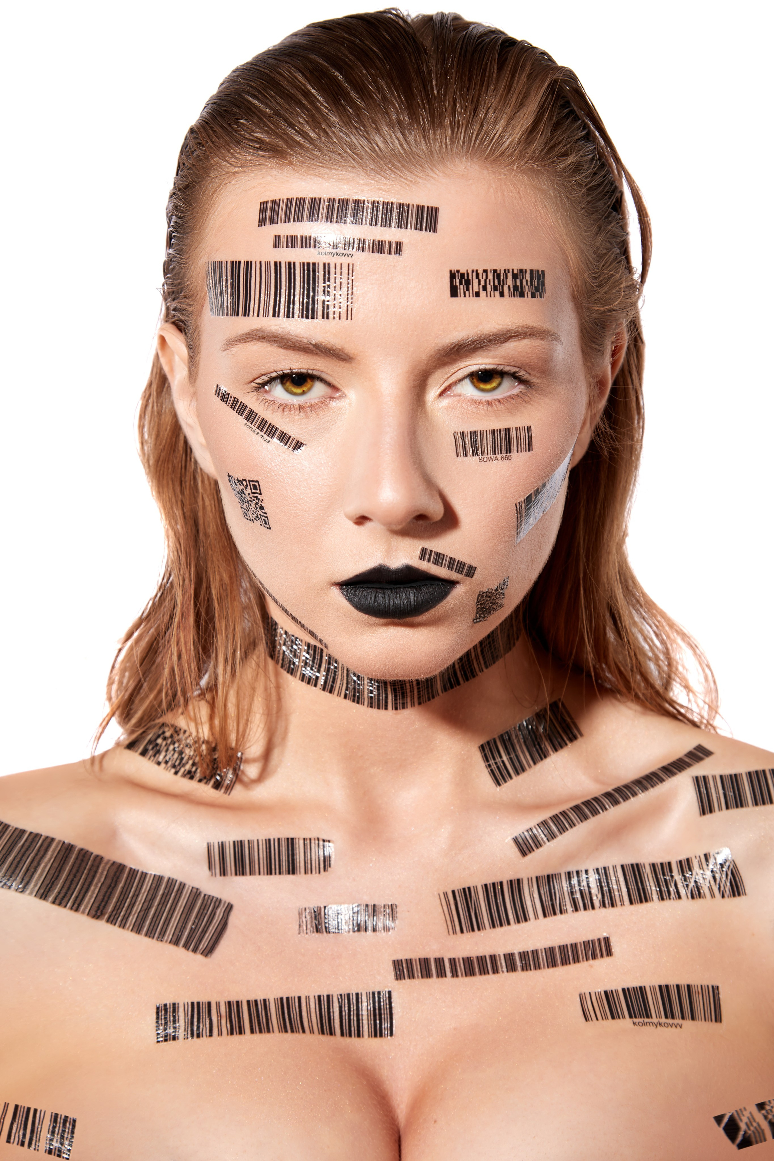 Съёмка контента для проекта: женщина с короткими светлыми волосами, покрытая штрих-кодами, которые покрывают её лицо, шею и плечи. Модель с чёрными губами и серьёзным выражением лица, на белом фоне. Художественная концепция, подчёркивающая тему идентичности и потребительского общества