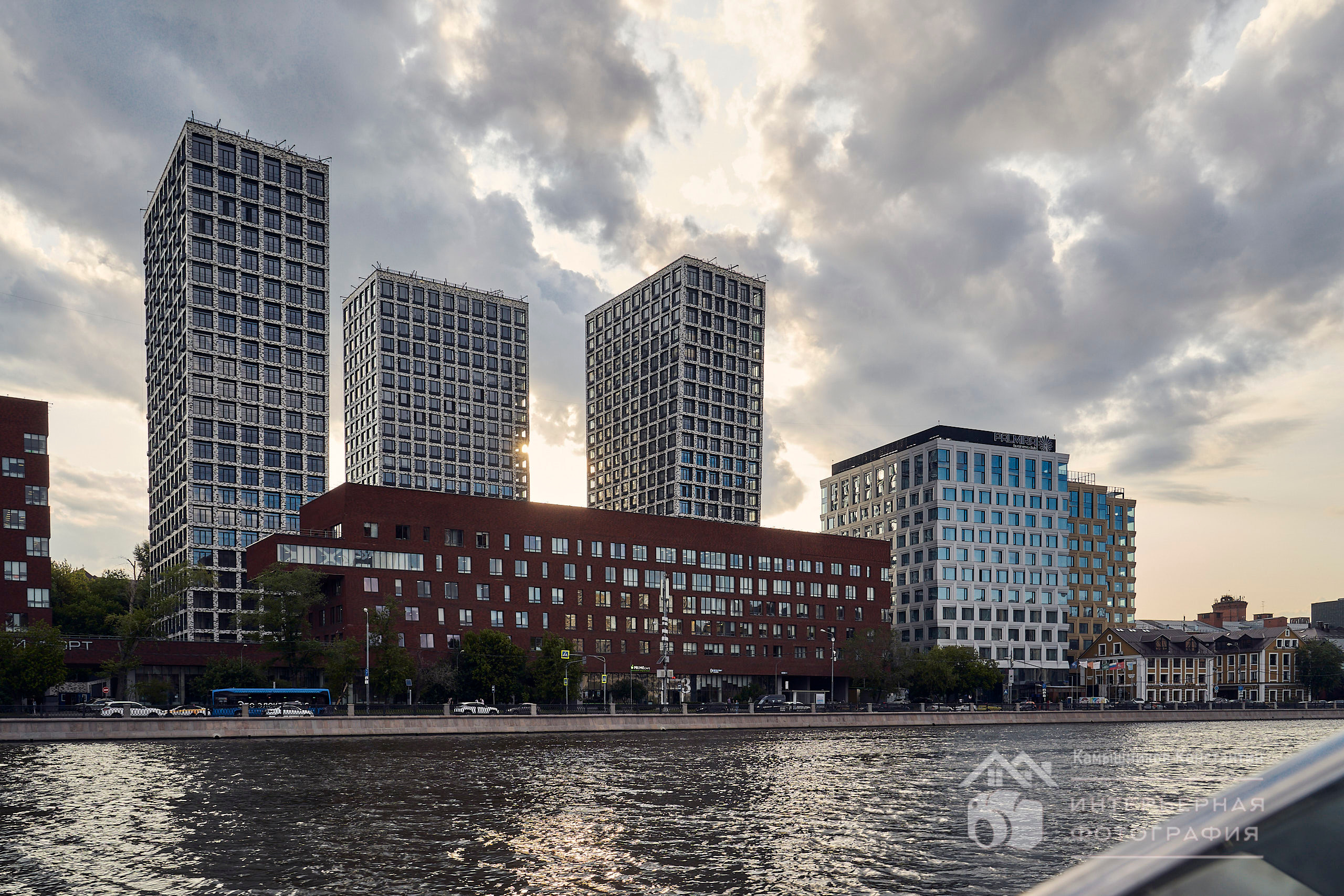 Архитектурное фото строящегося комплекса, вид с реки на городской пейзаж с суровым небом и лучами закатного солнца