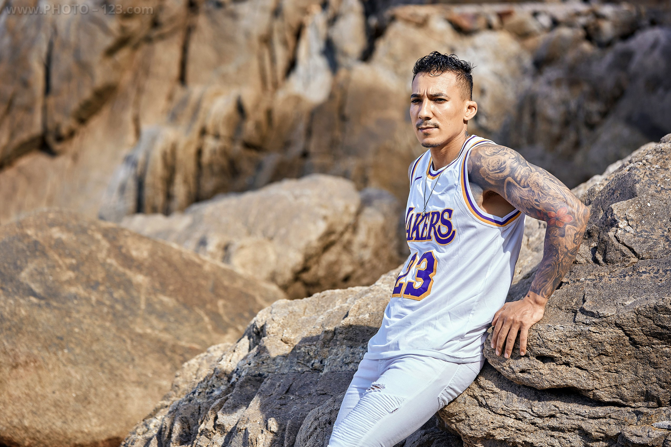 Tattooed muscular man posing against beach rocks during a male portrait session in Nha Trang