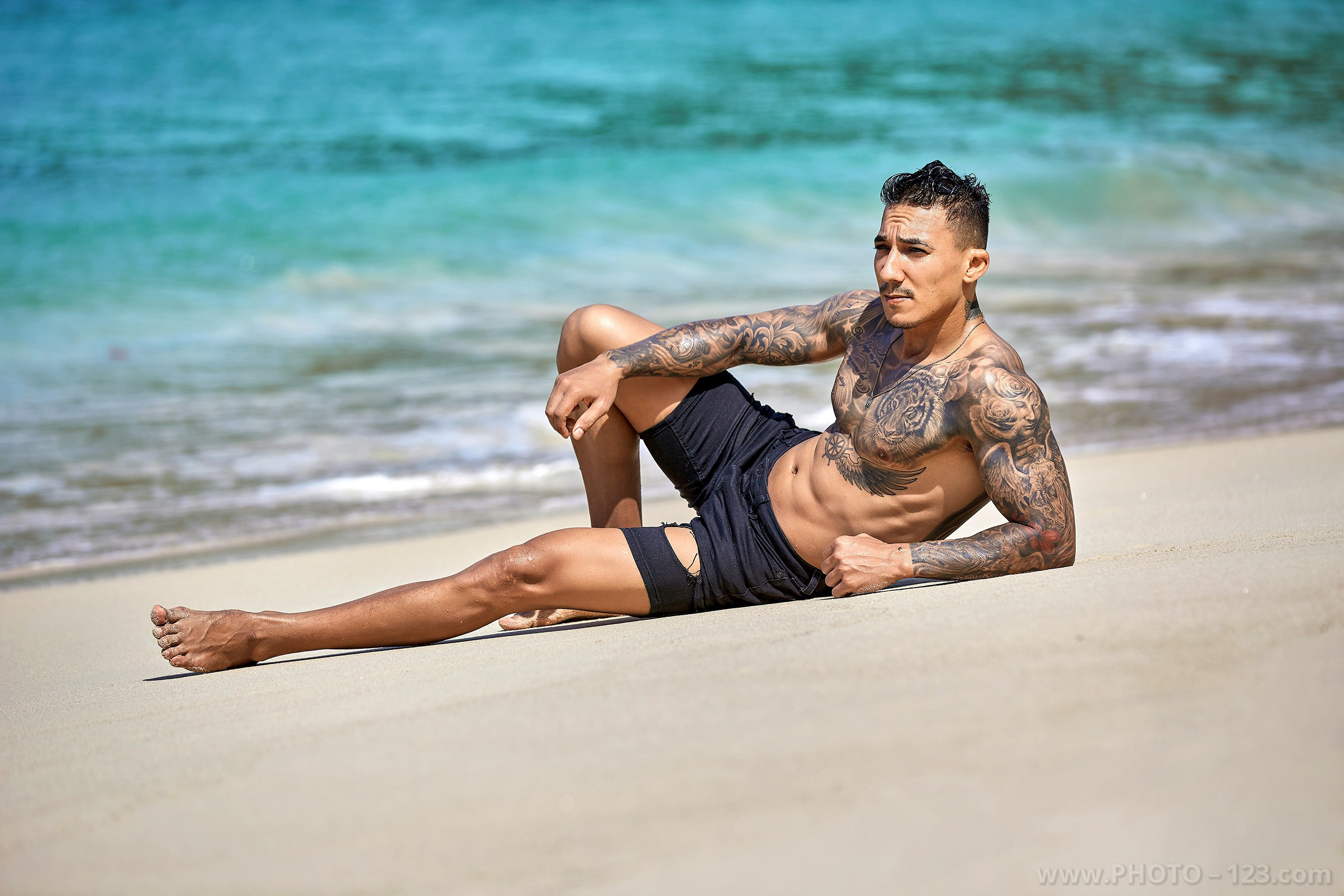 Tattooed fitness model lying on white sand near turquoise water during a Nha Trang photoshoot