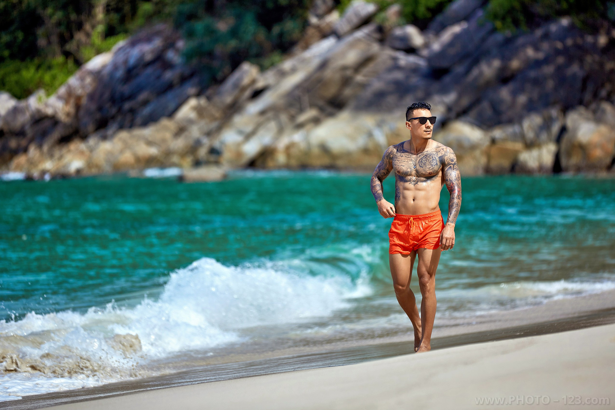 Athletic man in sunglasses and orange swim shorts strolling on the beach captured by Nha Trang photographer