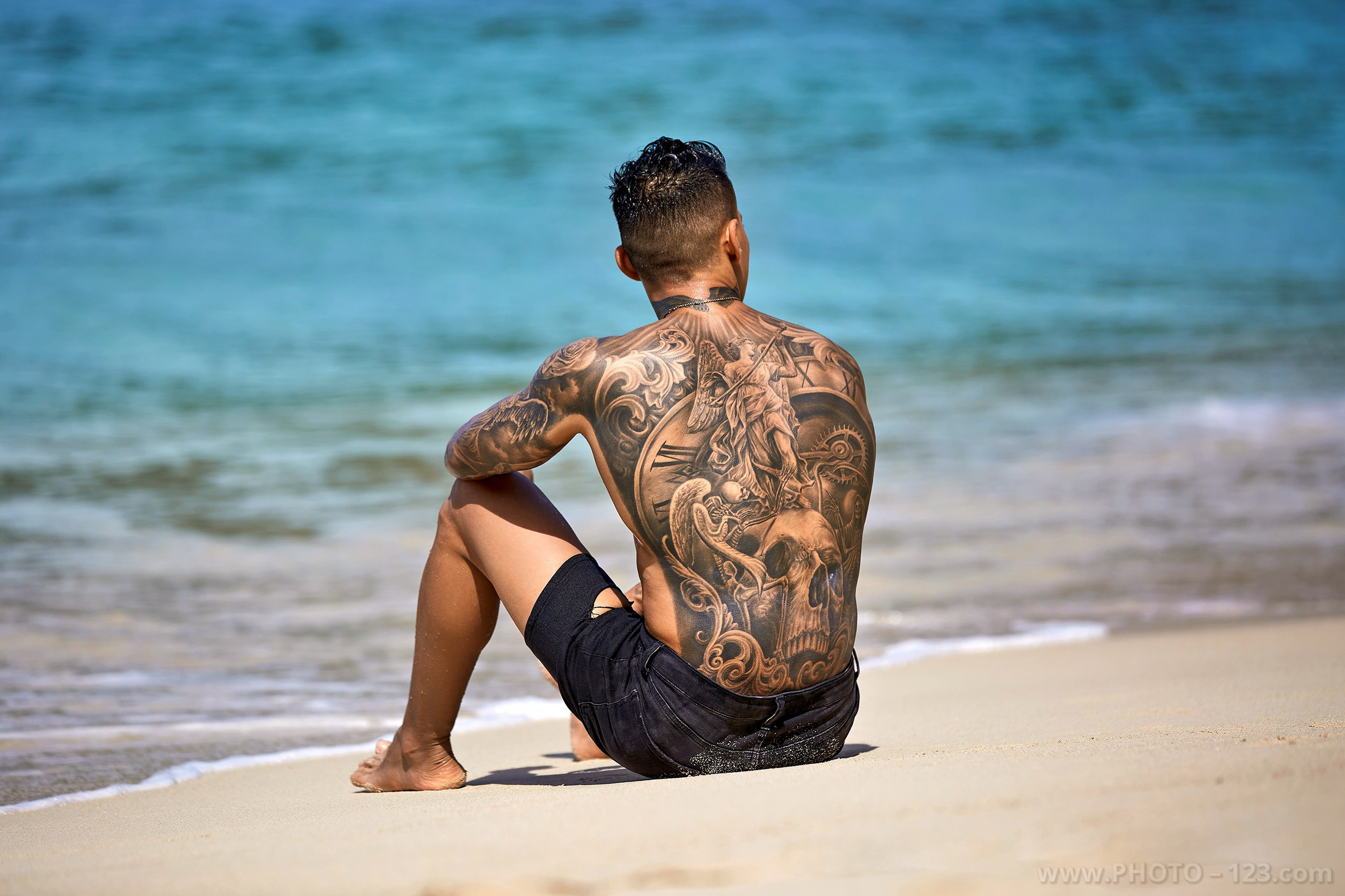 Back view of a tattooed man sitting on the beach shore in Nha Trang by local photographer