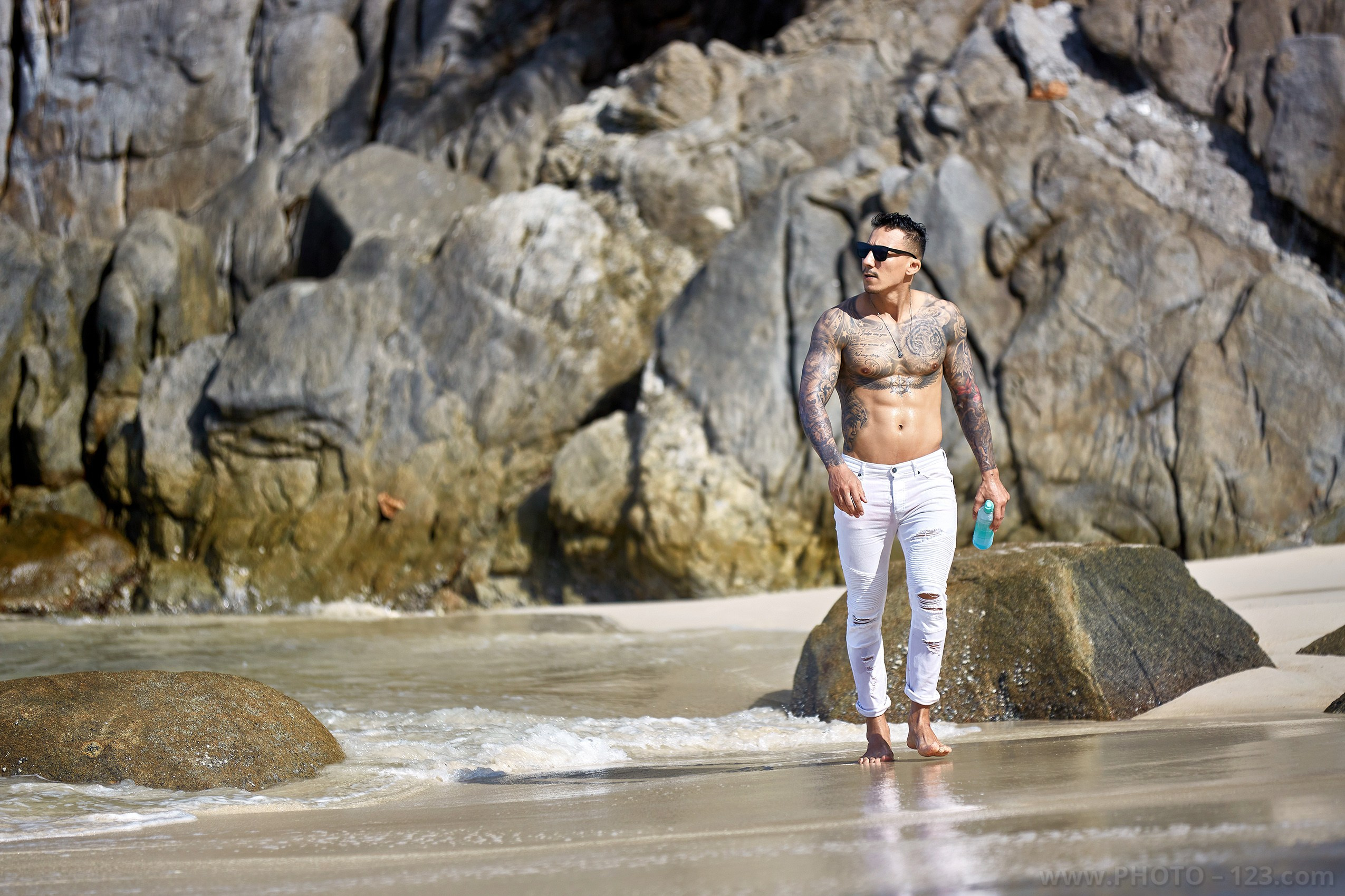 Tattooed fitness male model walking along the shoreline on a rocky Nha Trang beach