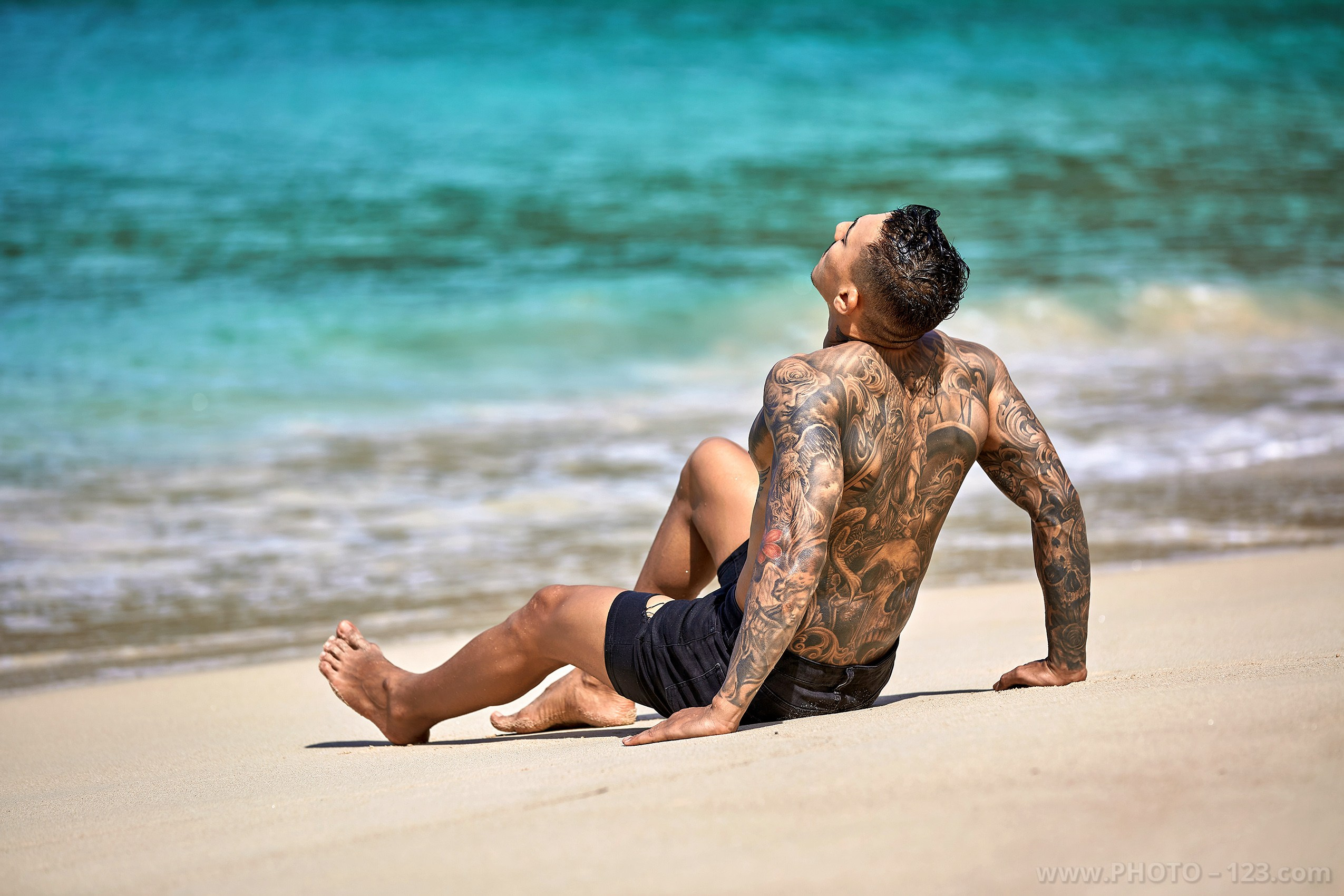 Tattooed male model leaning back on white sand on a tropical Nha Trang beach