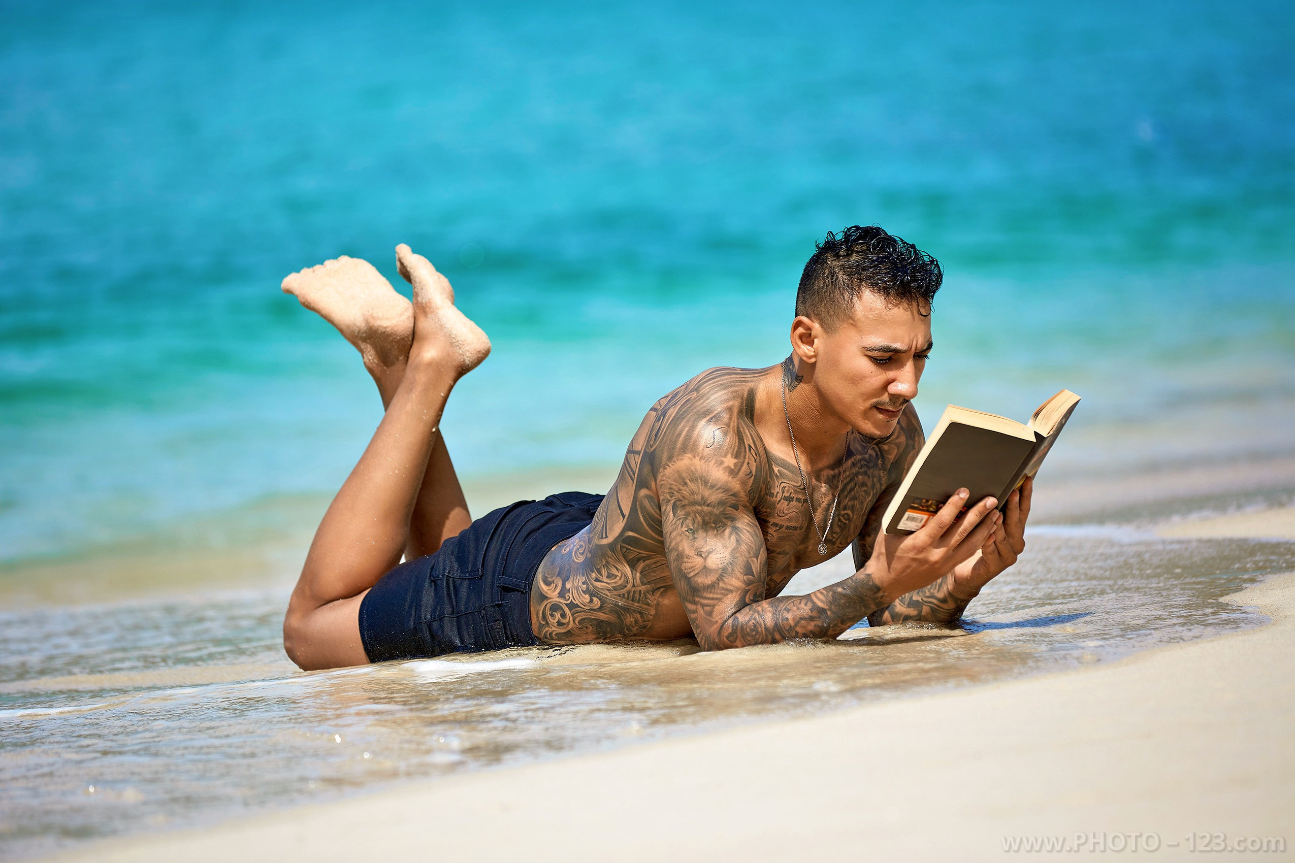 Shirtless athletic man lying on the shore reading a book on a Nha Trang beach