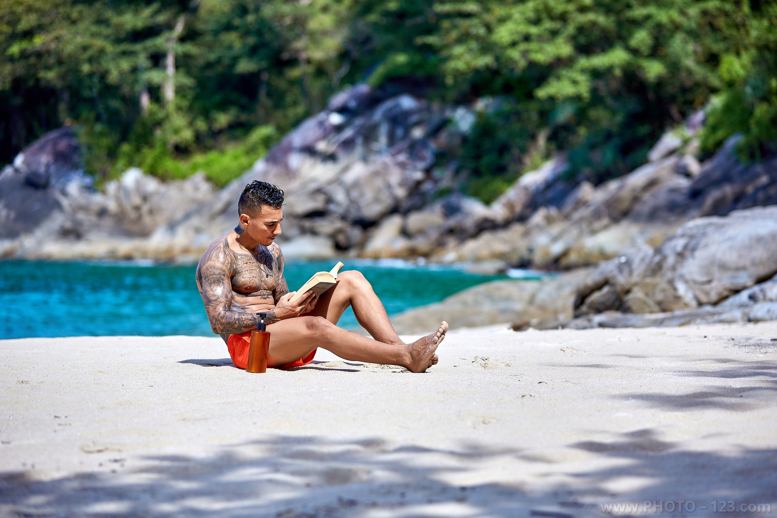 Shirtless man reading a book on a sandy beach during a portrait session in Nha Trang