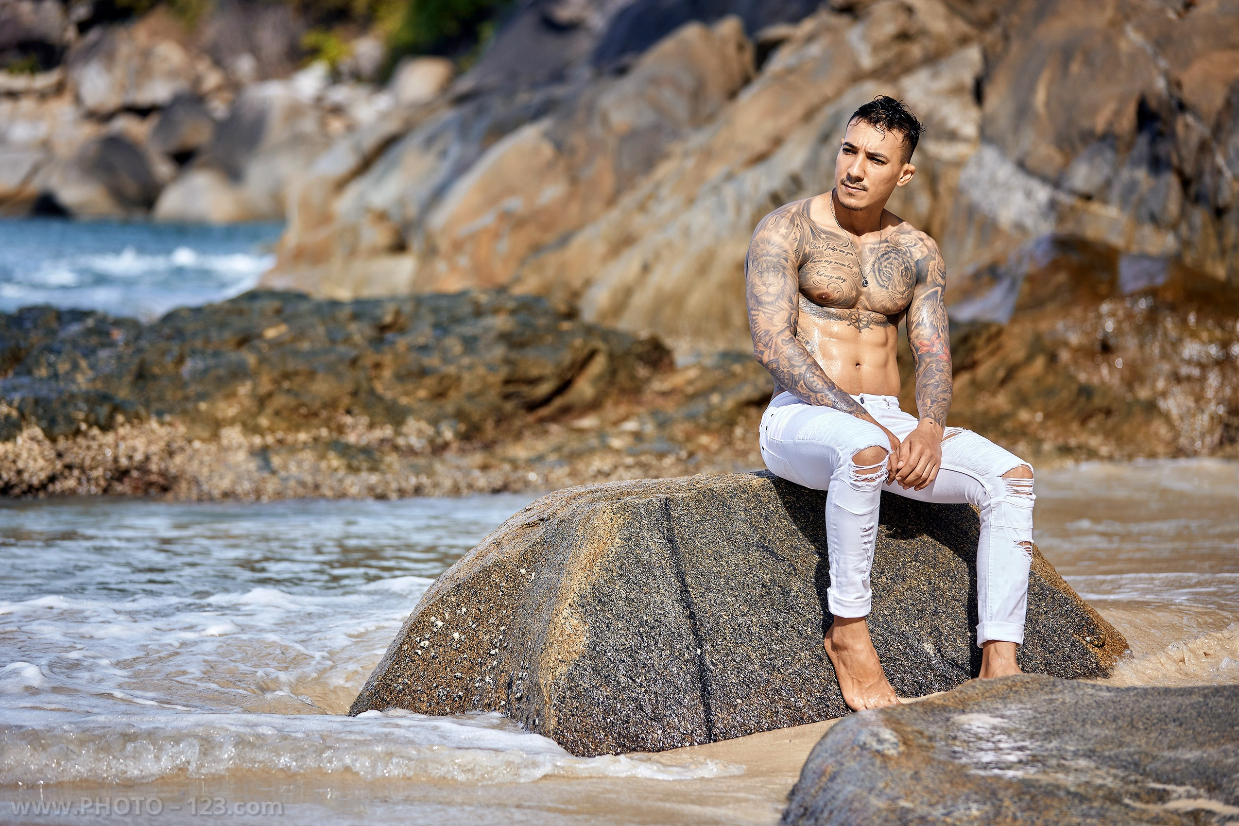 Shirtless tattooed man sitting on an ocean rock during a male fitness photoshoot in Nha Trang by local photographer