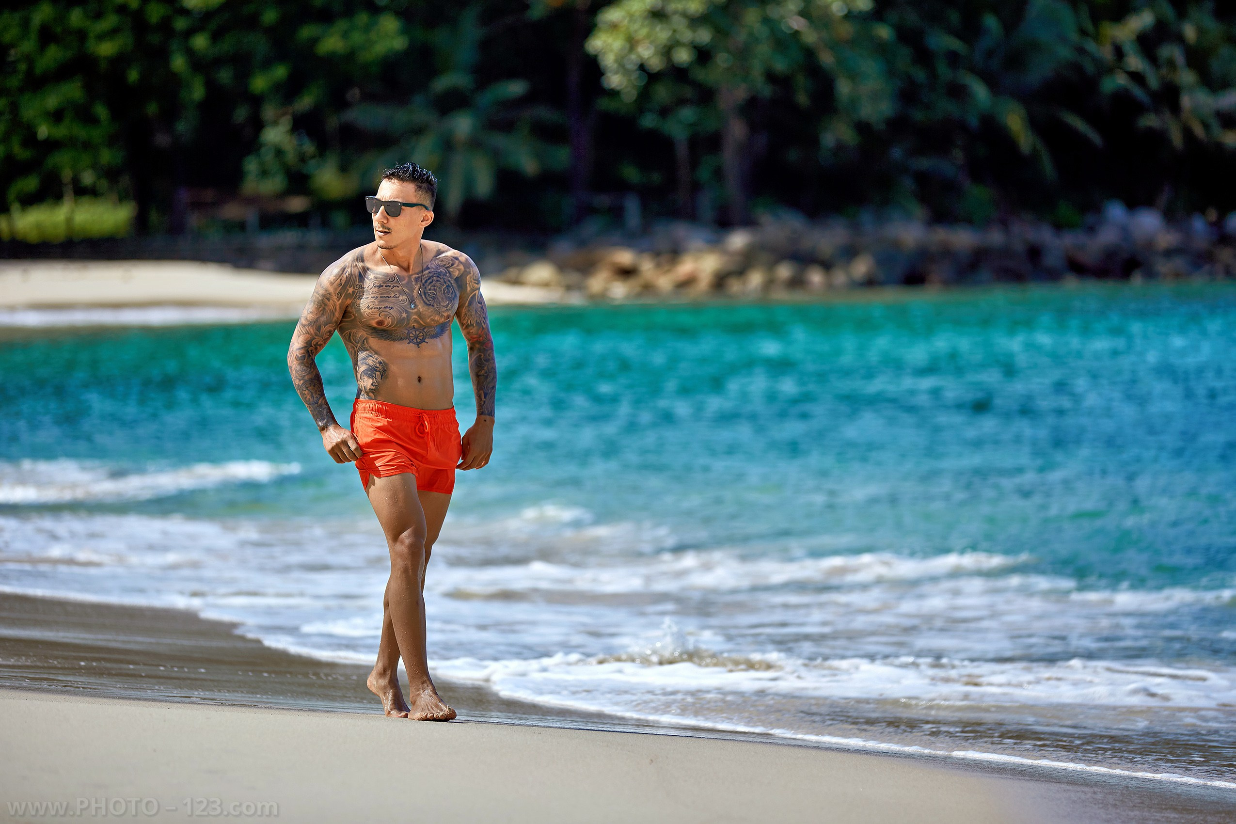 Shirtless muscular model in orange shorts walking on a tropical beach in Nha Trang Vietnam