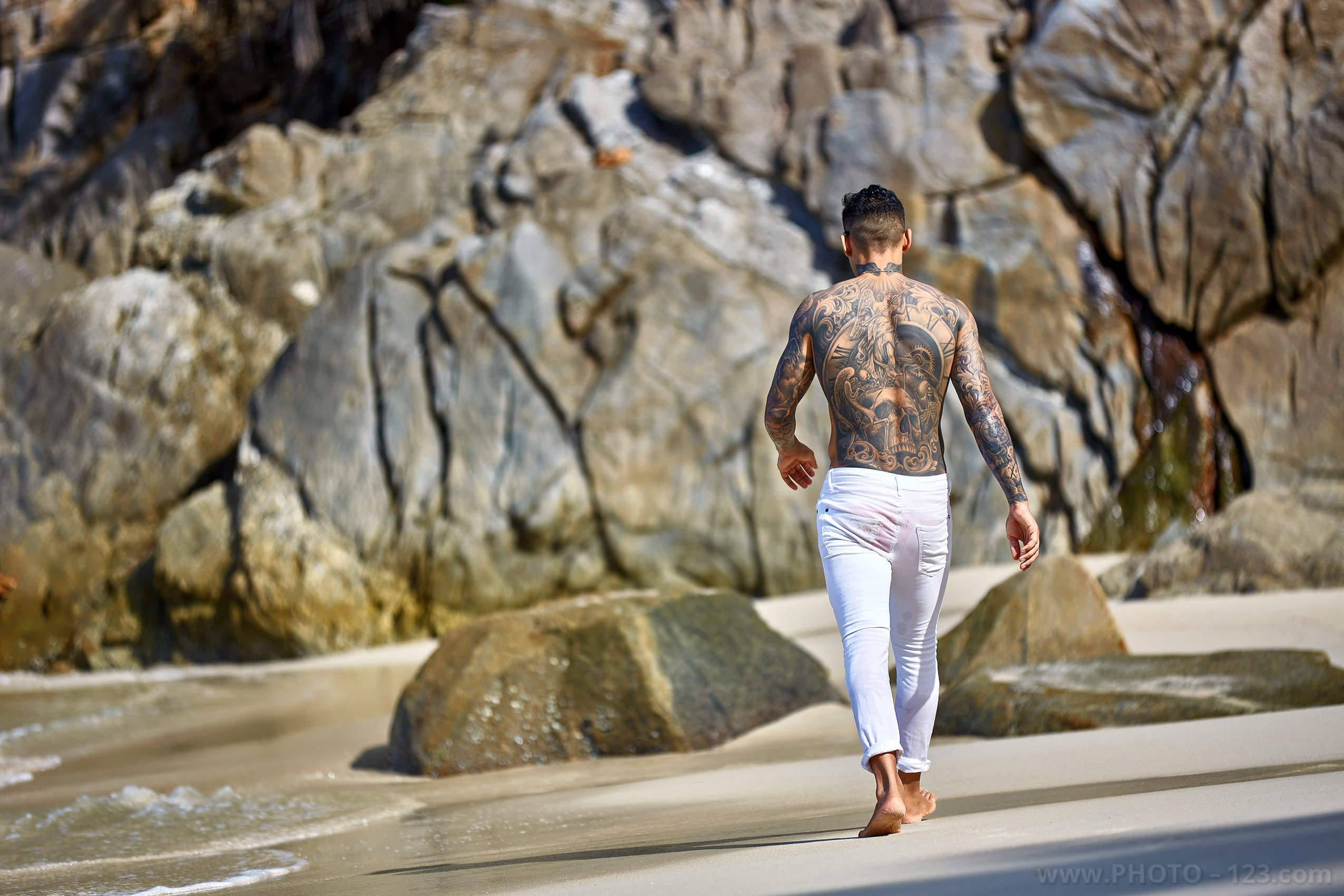 Back view of a tattooed athletic man walking towards coastal rocks in Nha Trang Vietnam