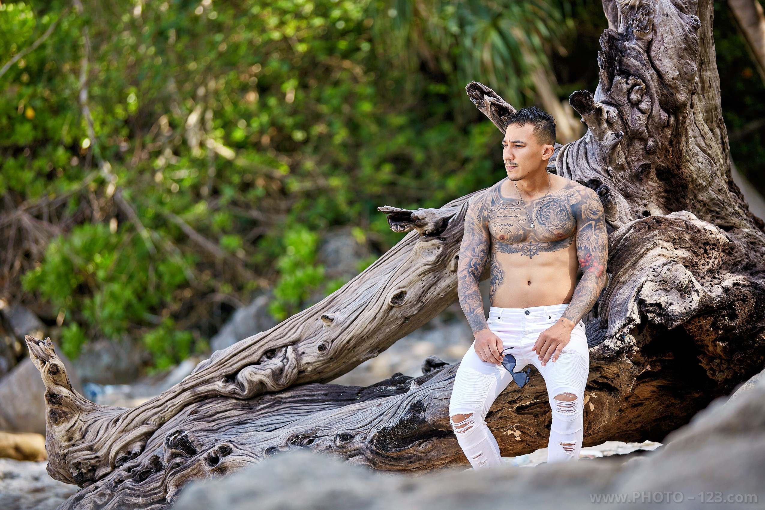 Athletic male model sitting on coastal driftwood during a fitness photoshoot by Nha Trang photographer