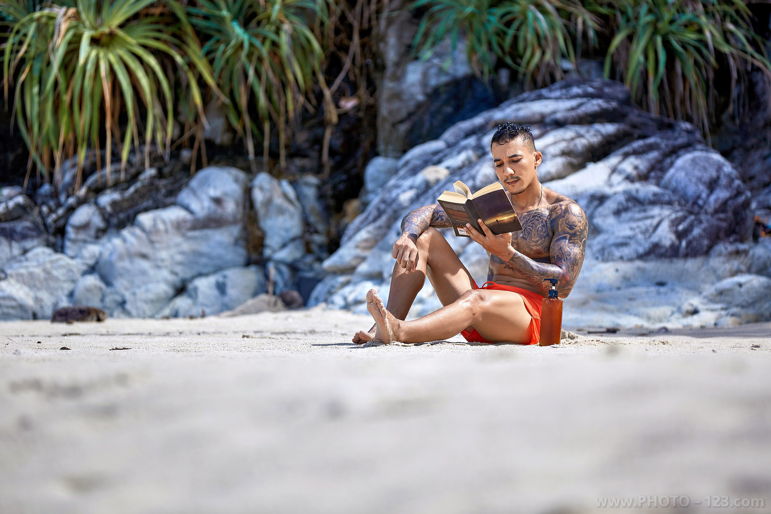 Muscular man sitting on white sand reading a book on a tropical beach in Nha Trang