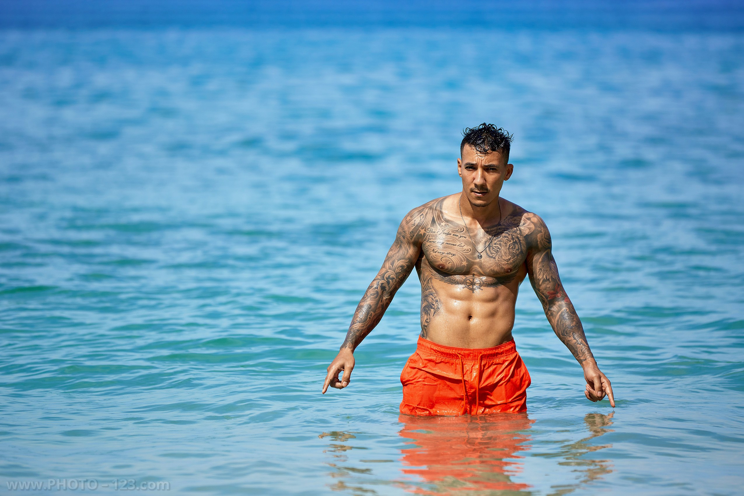 Muscular man in orange swim shorts standing waist-deep in turquoise ocean water in Nha Trang