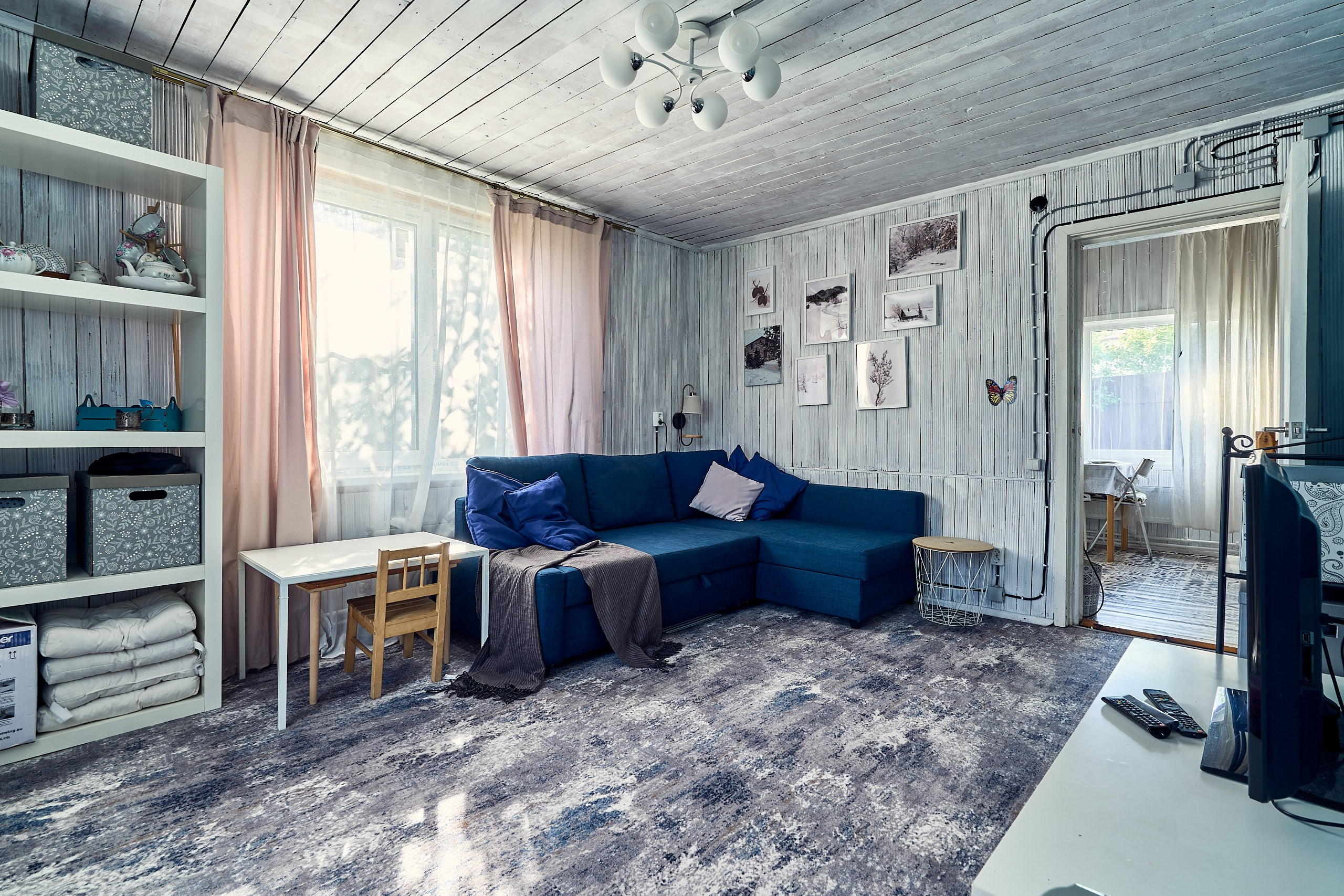 Интерьерная фотография гостиной дома в Подмосковье с окном, диваном, ковром и открытой дверью в кухню-прихожую