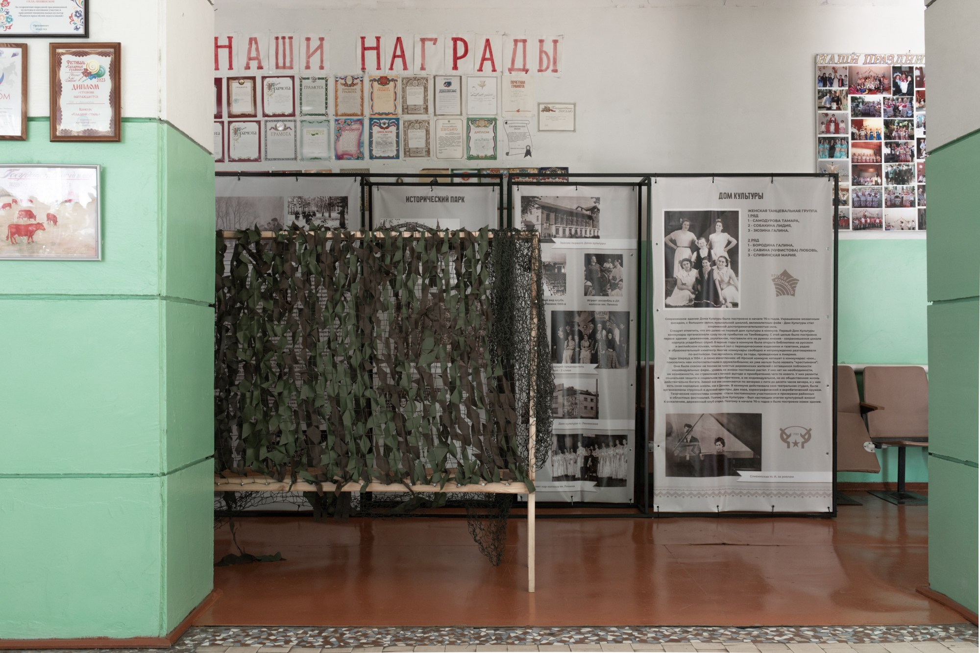 В коридоре Дома культуры грамоты, полученные ДК и его сотрудниками, соседствуют с маскировочными сетями, которые жители плетут для нужд СВО.