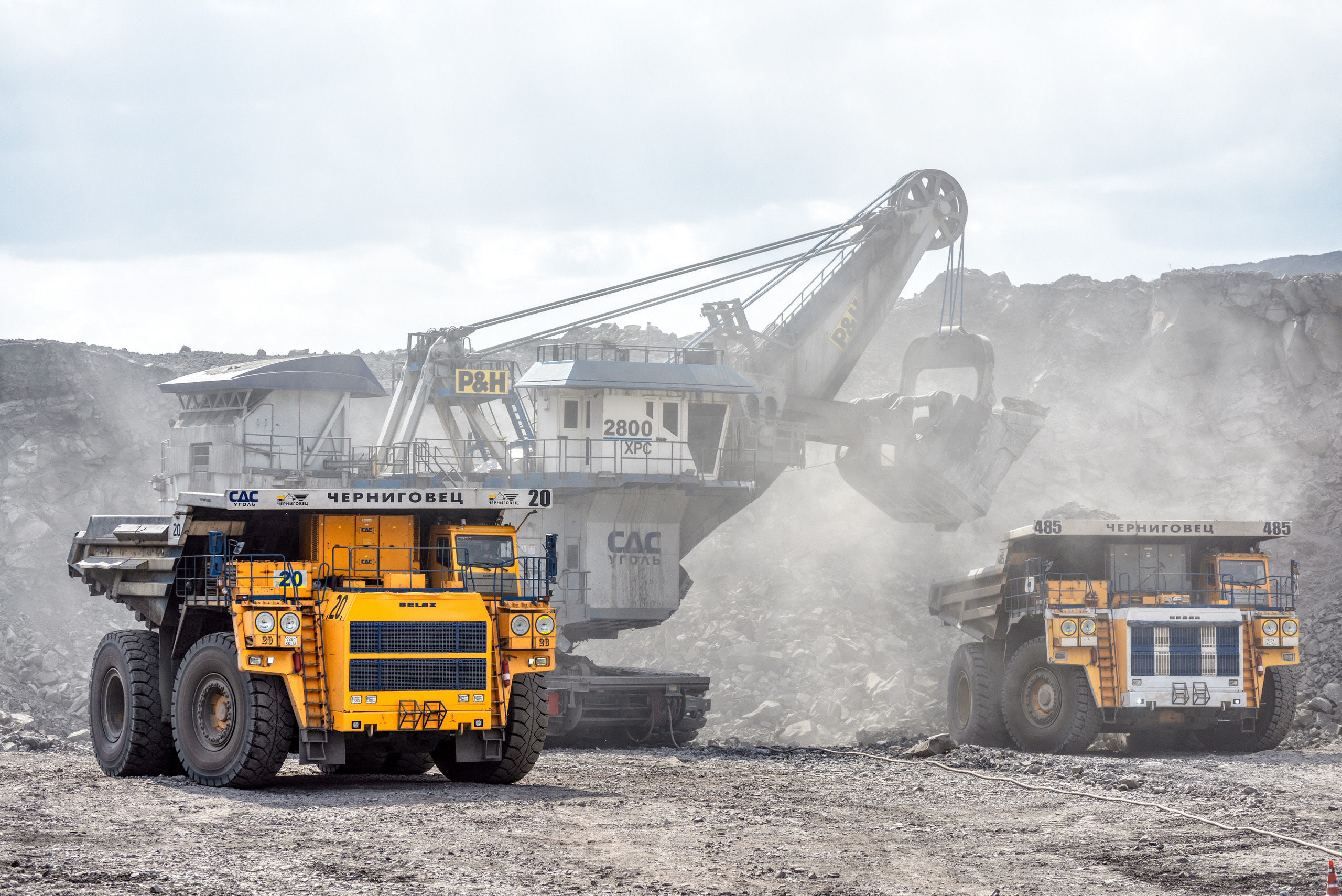 Мощный экскаватор грузит уголь в карьерные самосвалы. Добыча каменного угля открытым способом.
