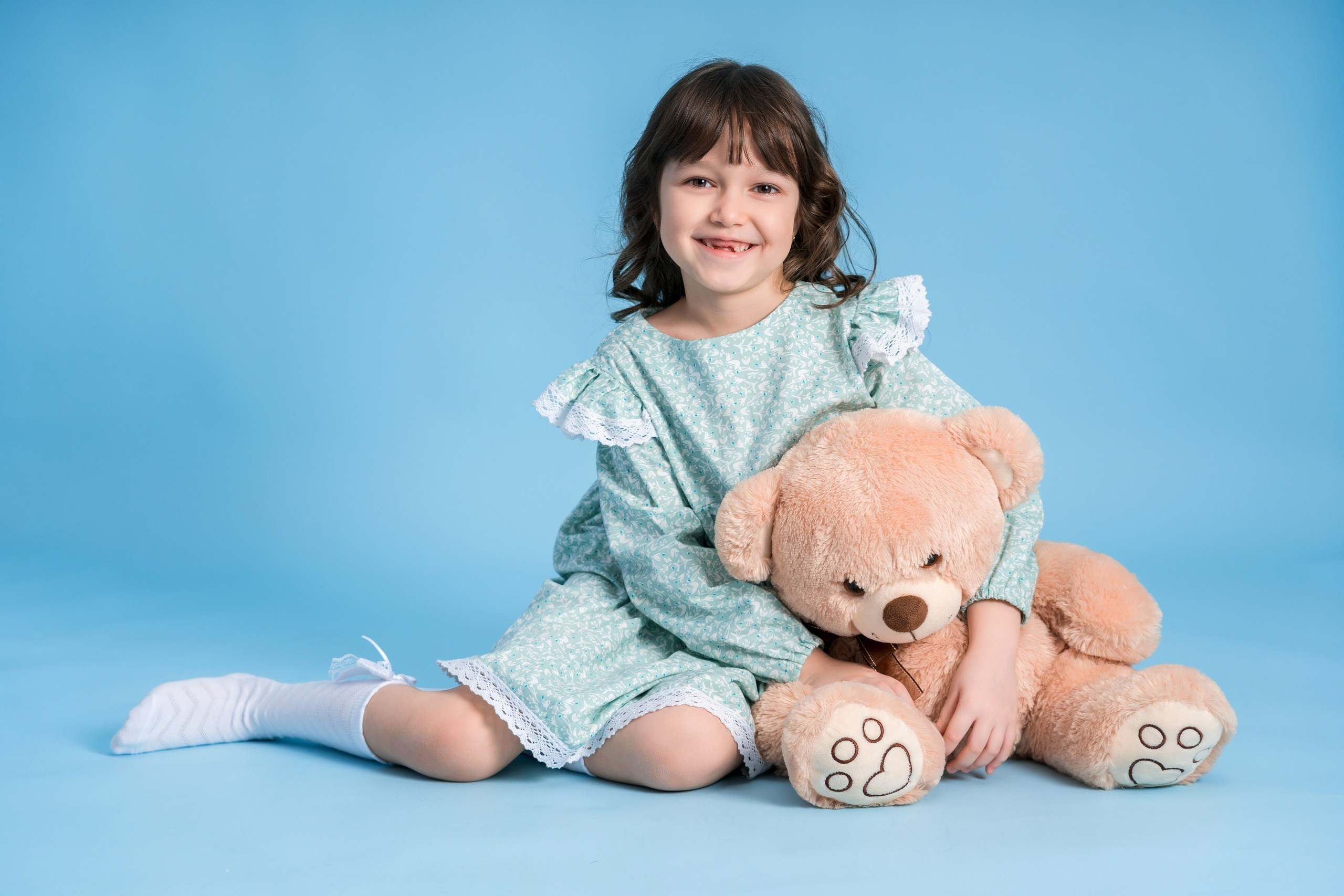 Девочка на синем фоне обнимает медведя, фотосессия в студии
