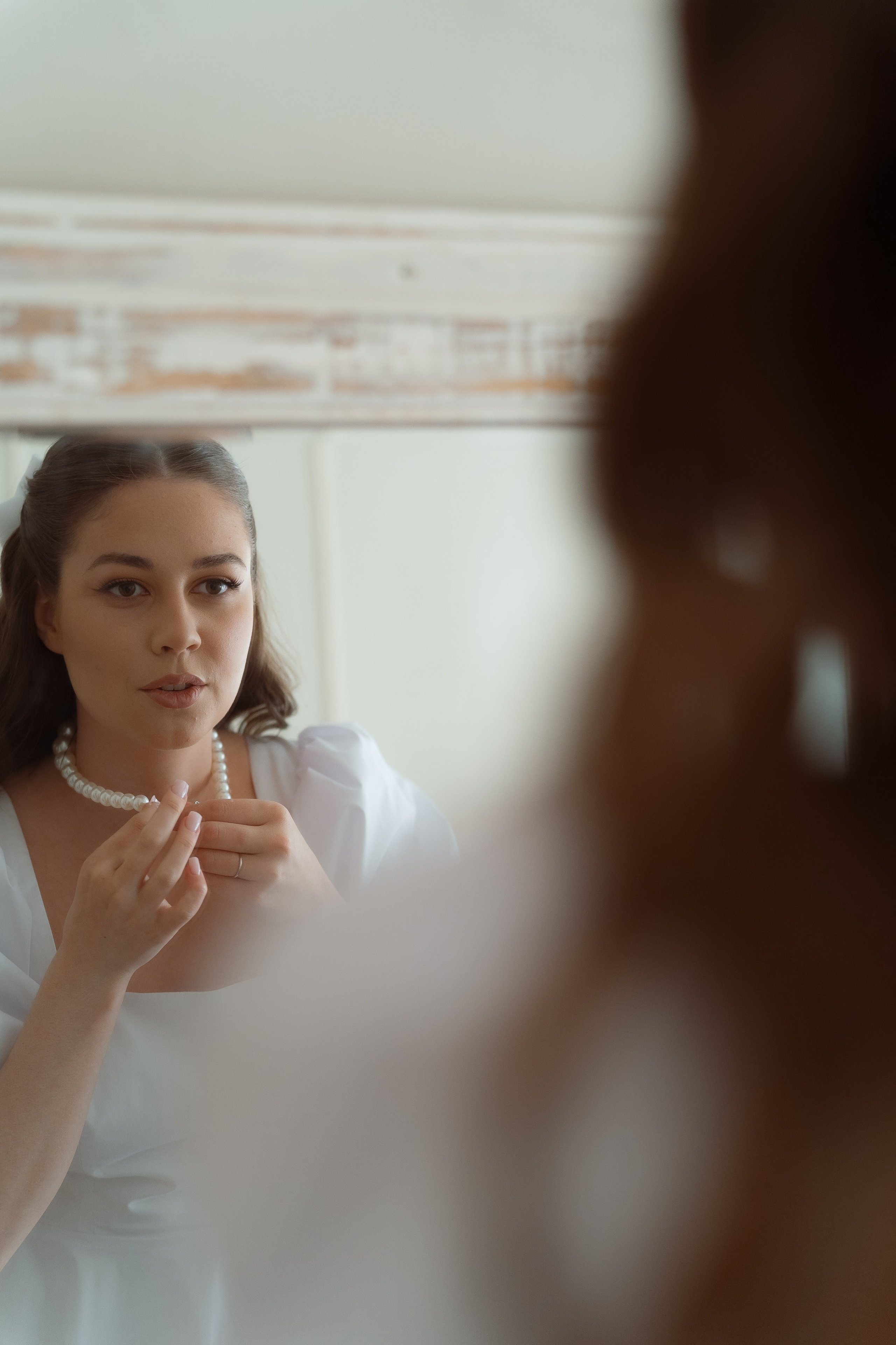 Невеста красит губы перед зеркалом, естественная свадебная фотосессия