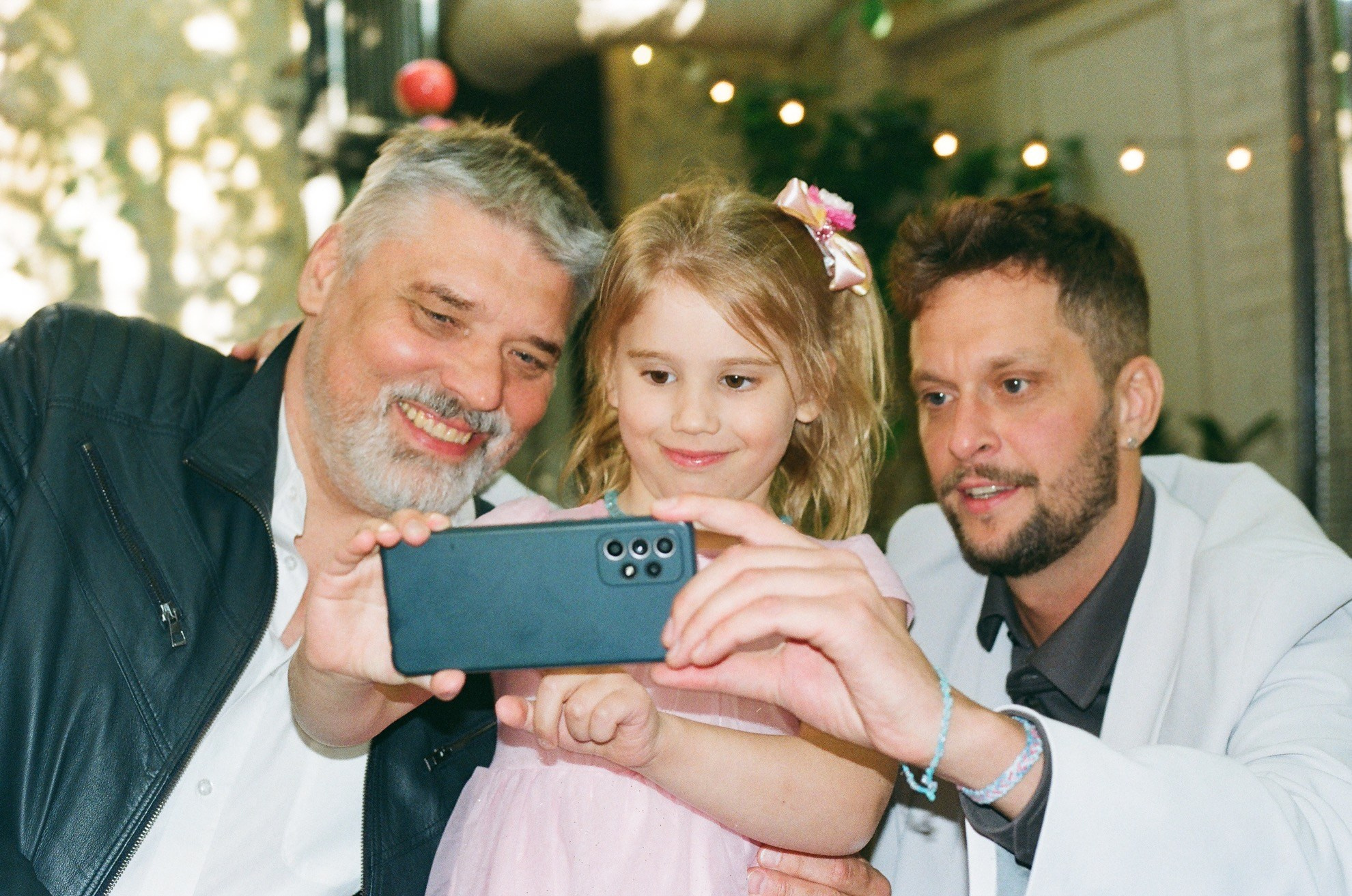 Плёночное фото: гости свадьбы делают селфи с девочкой в праздничной атмосфере