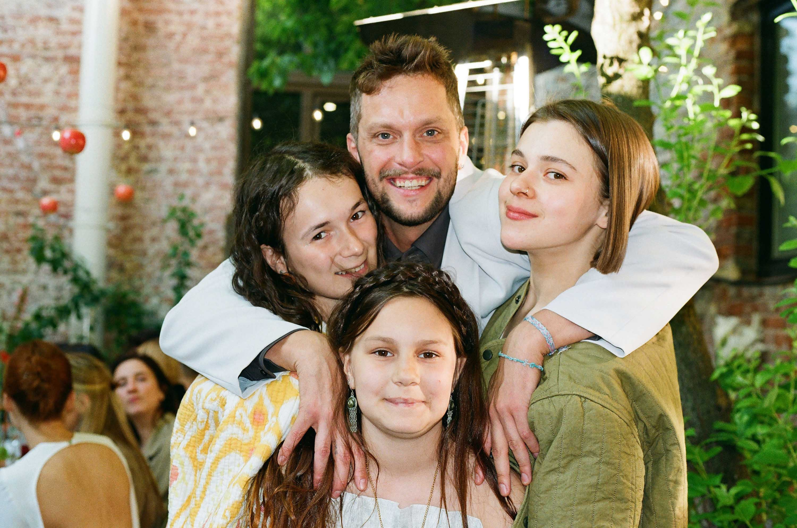 Тёплые семейные объятия гостей свадьбы у кирпичной стены, кадр на плёнку