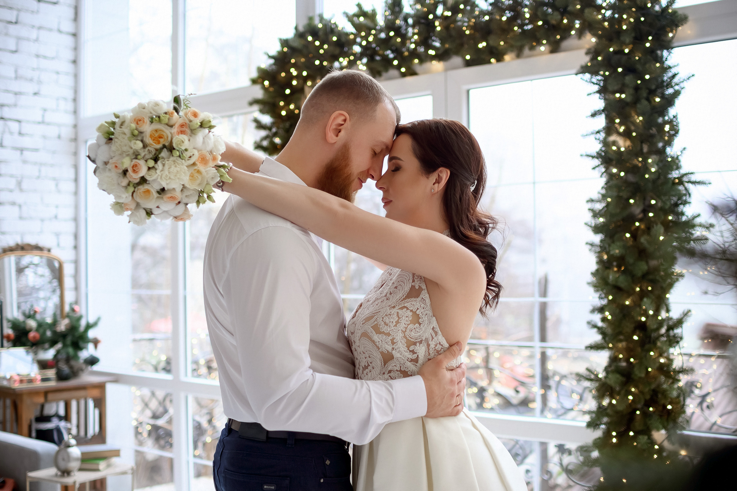 Двое молодоженов в новогодней фотостудии со светлым интерьером.