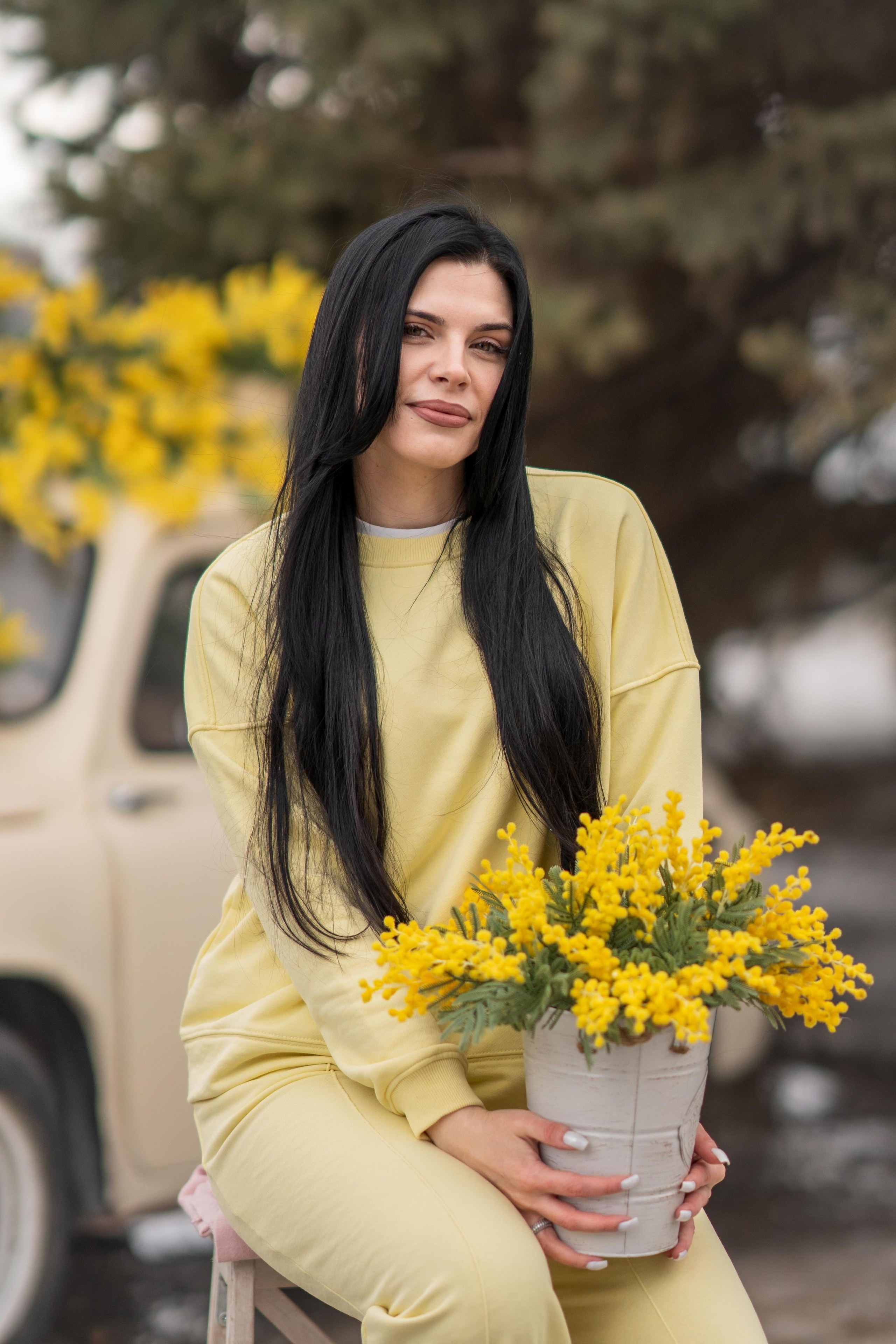 Девушка с букетом мимозы на фоне бежевой ретро машинки