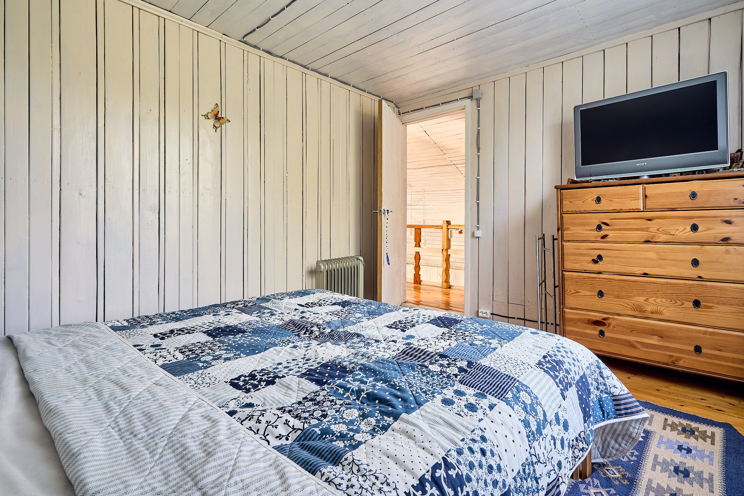 Интерьерное фото общего вида спальни с кроватью, телевизором и дверью на балкон мезонина