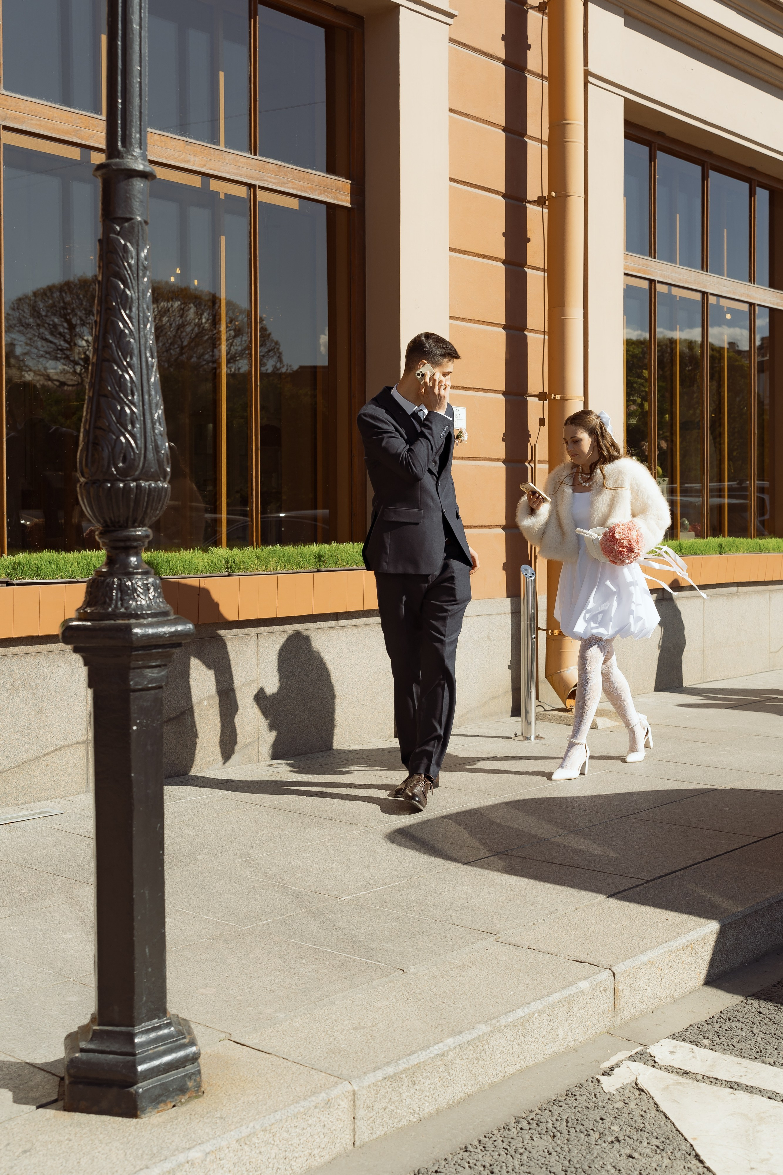 Жених и невеста идут по солнечным улицам Петербурга рядом с витринами отеля