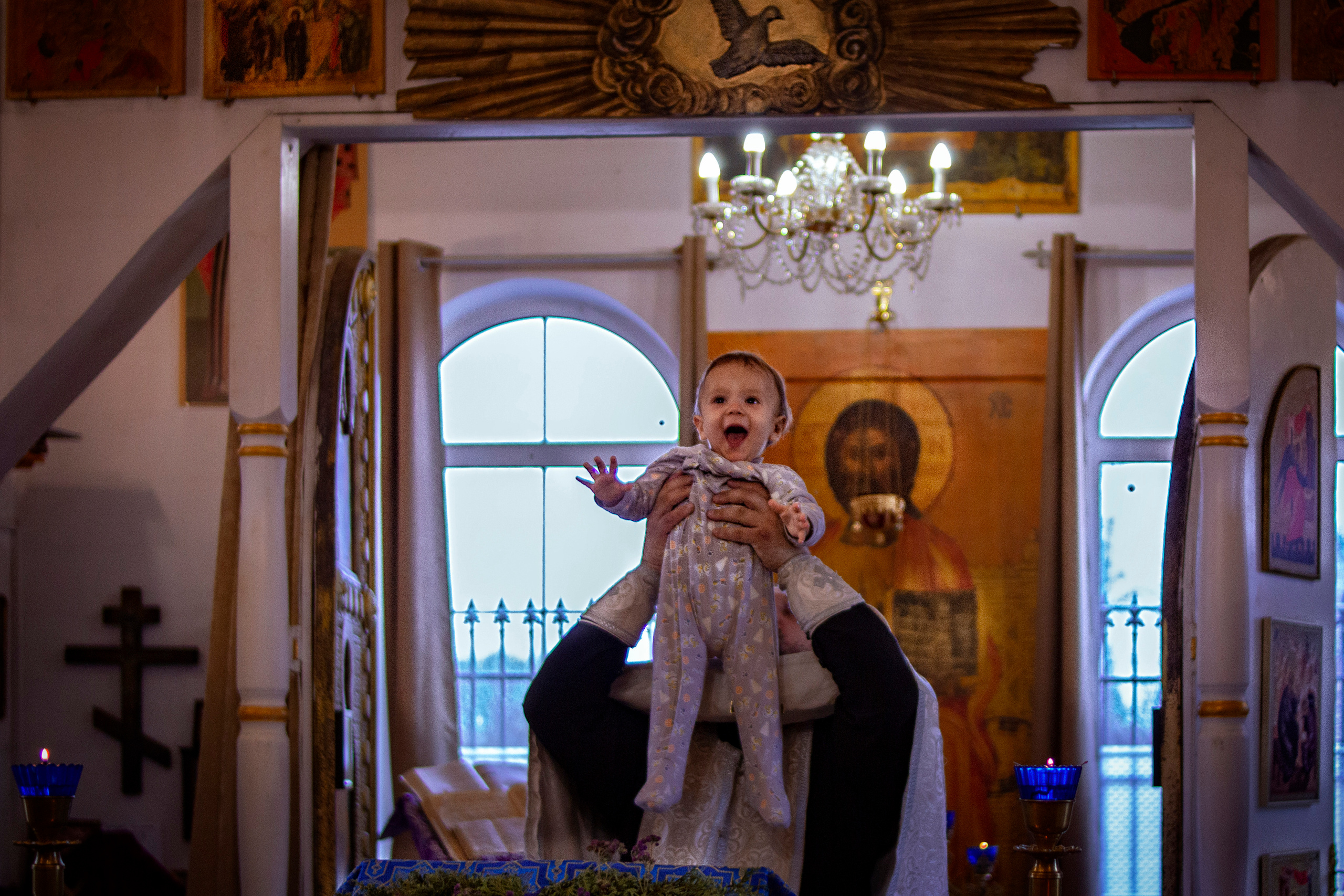 Батюшка выносит из алтаря младенца на руках в процессе крещения