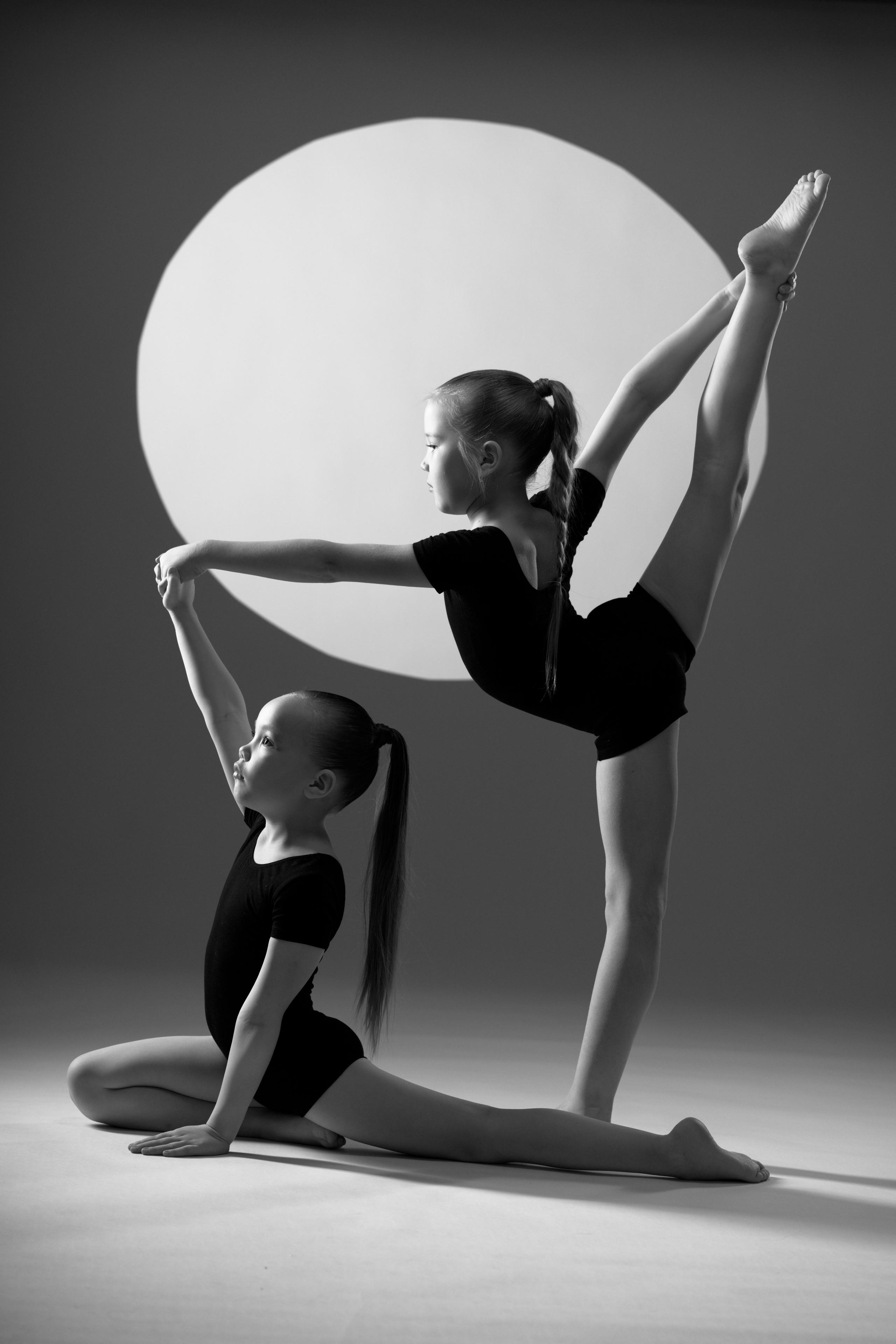 Черно-белое фото юных гимнасток в парной позе: вертикальный шпагат в круге света, художественная гимнастика в Тюмени.