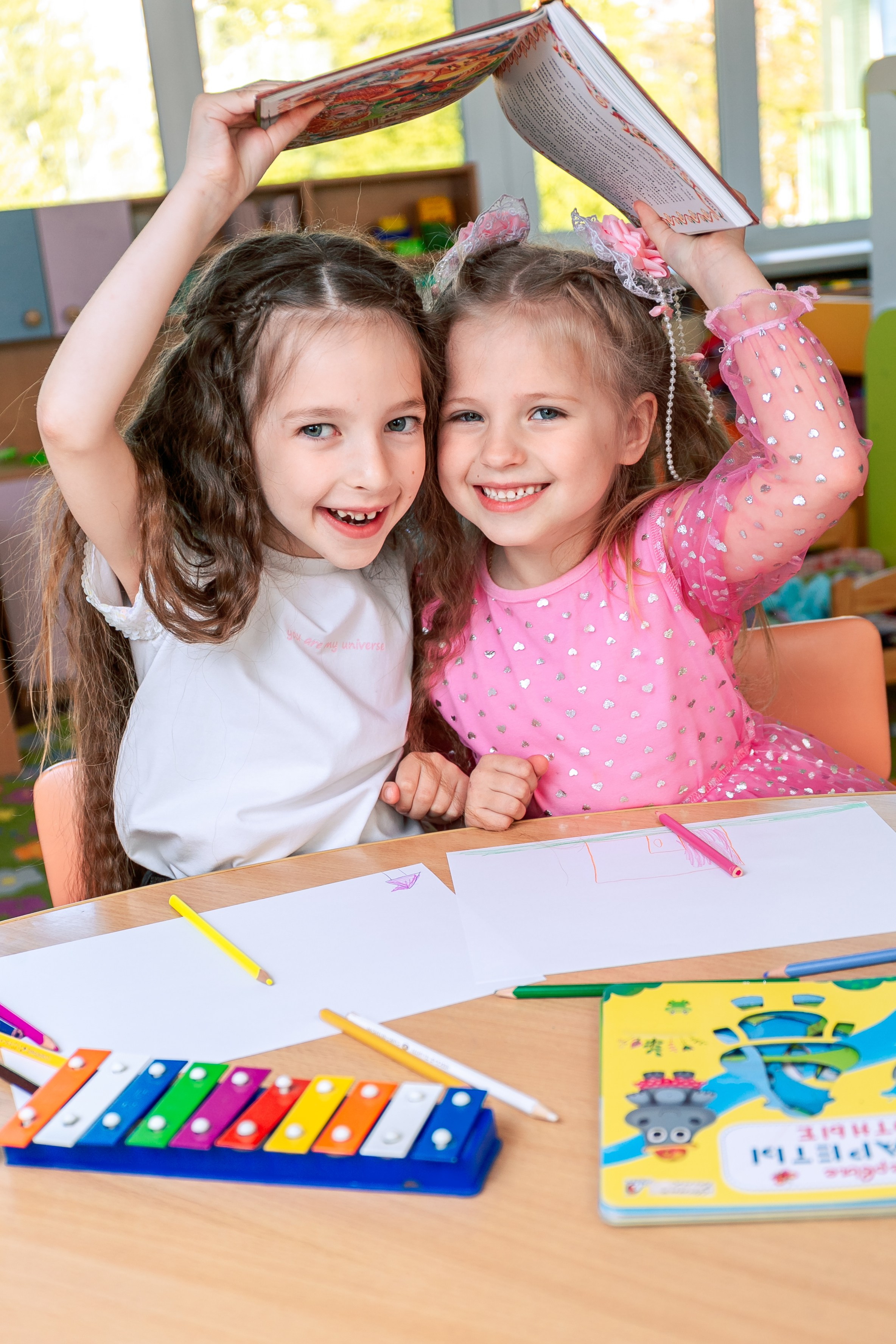 Весёлые девочки сидящие за столом с книгой в детском саду