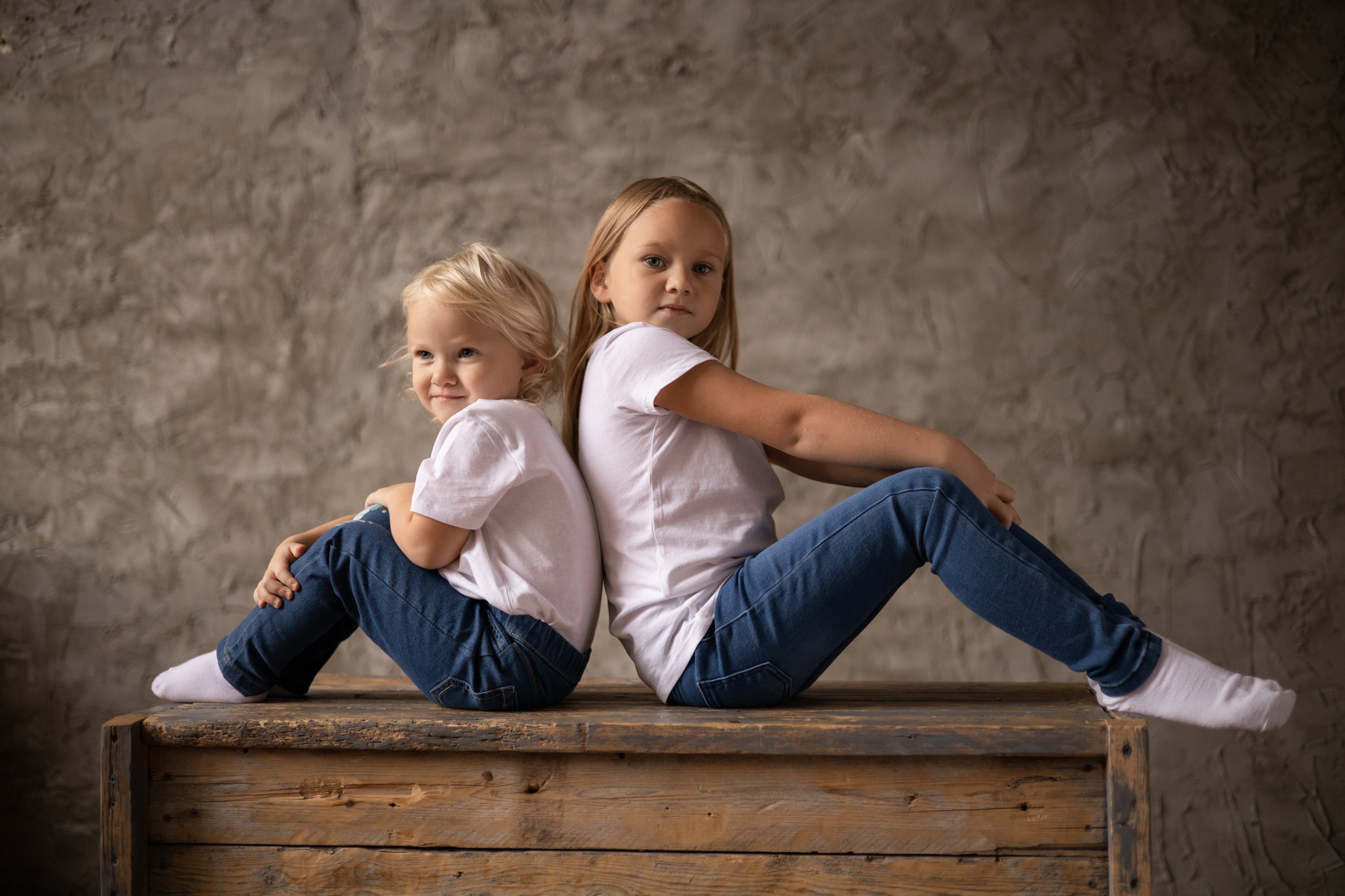 Двое детей сидят спиной друг к другу, ноги слегка согнуты в коленях. Семейная фотосессия Астрахань.