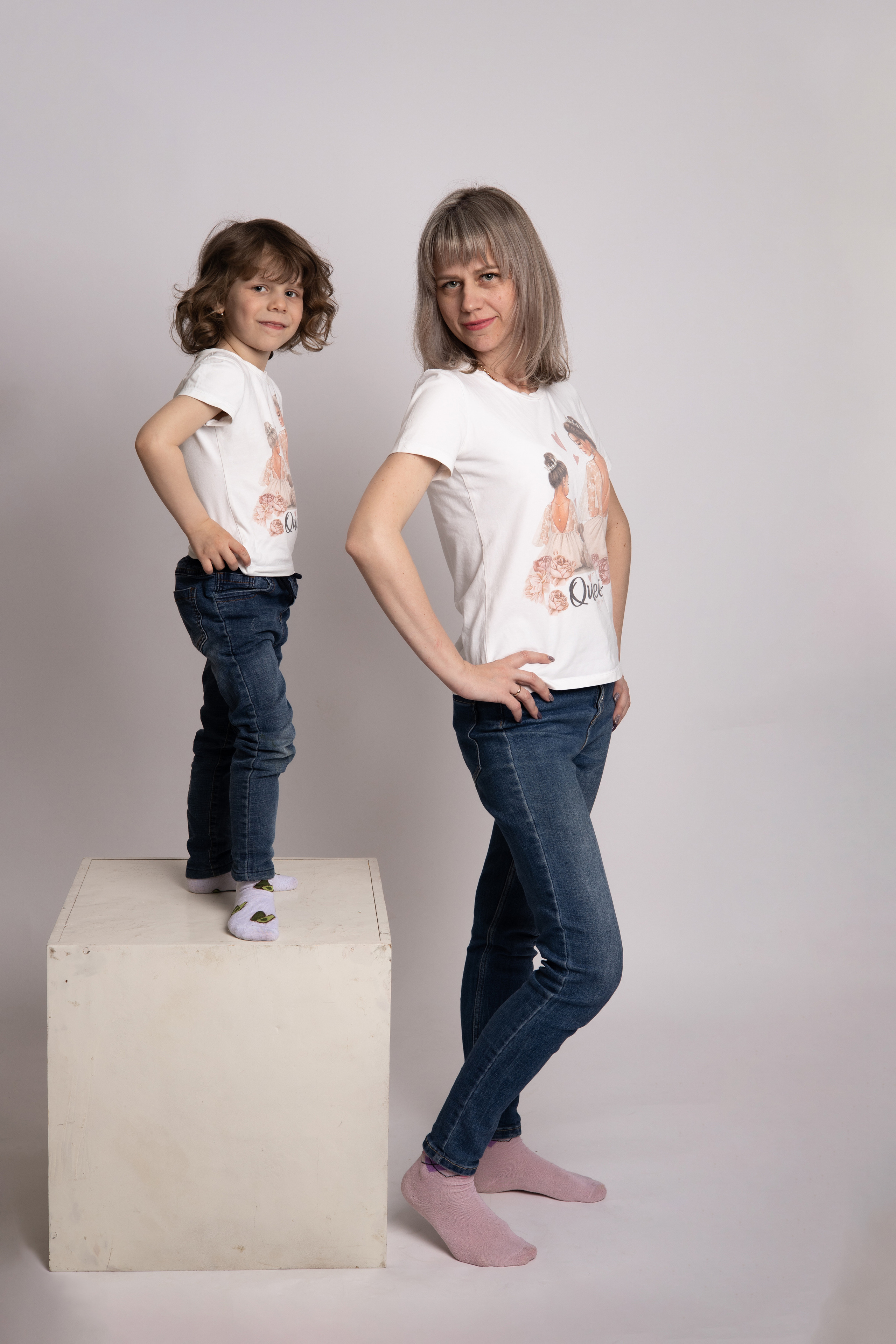 Мама и дочка, мама стоит на полу, дочка стоит на пуфе, руки у обеих на талии. Семейная фотосессия Астрахань.