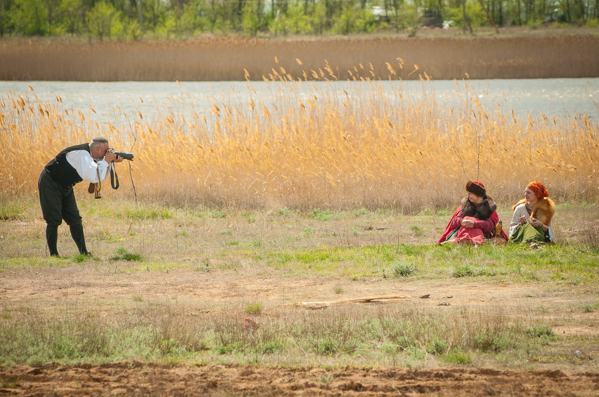 Фотограф фотографирует участников исторической реконструкции в поле на фоне зарослей камышей