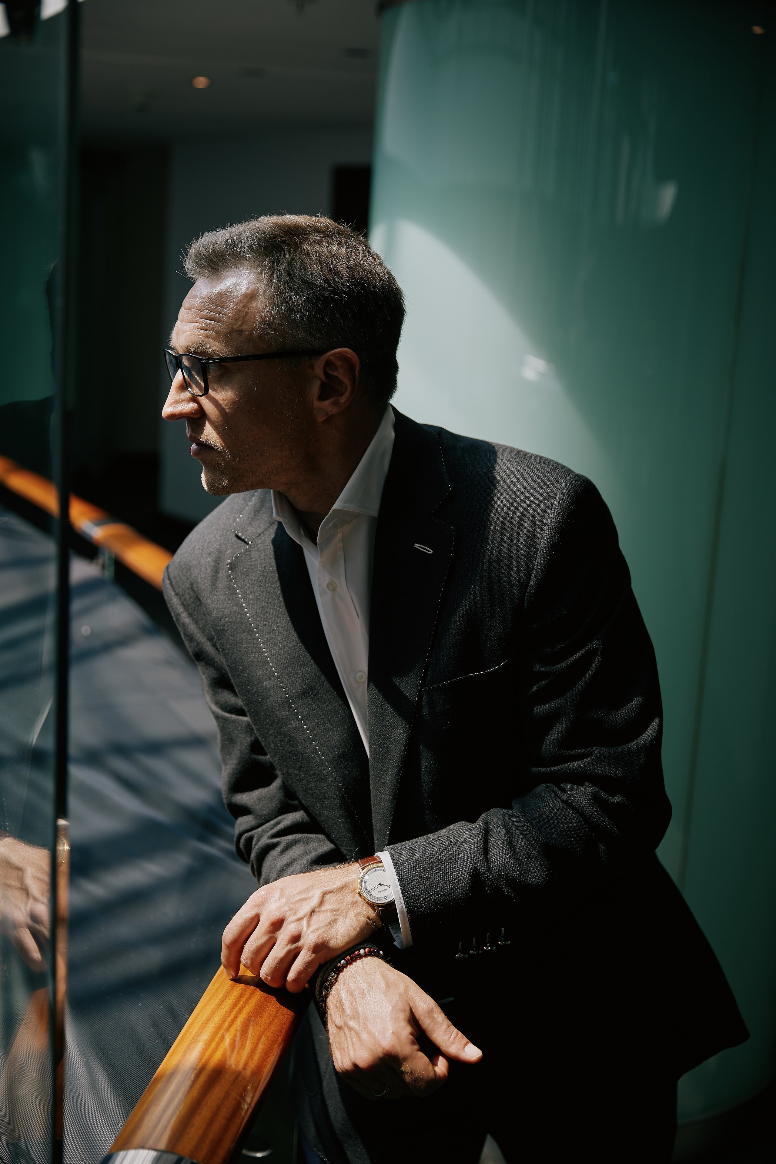 Деловой портрет руководителя на локации — мужчина в тёмном пиджаке облокотился на перила лестницы, непринуждённая поза, корпоративная съёмка в интерьере