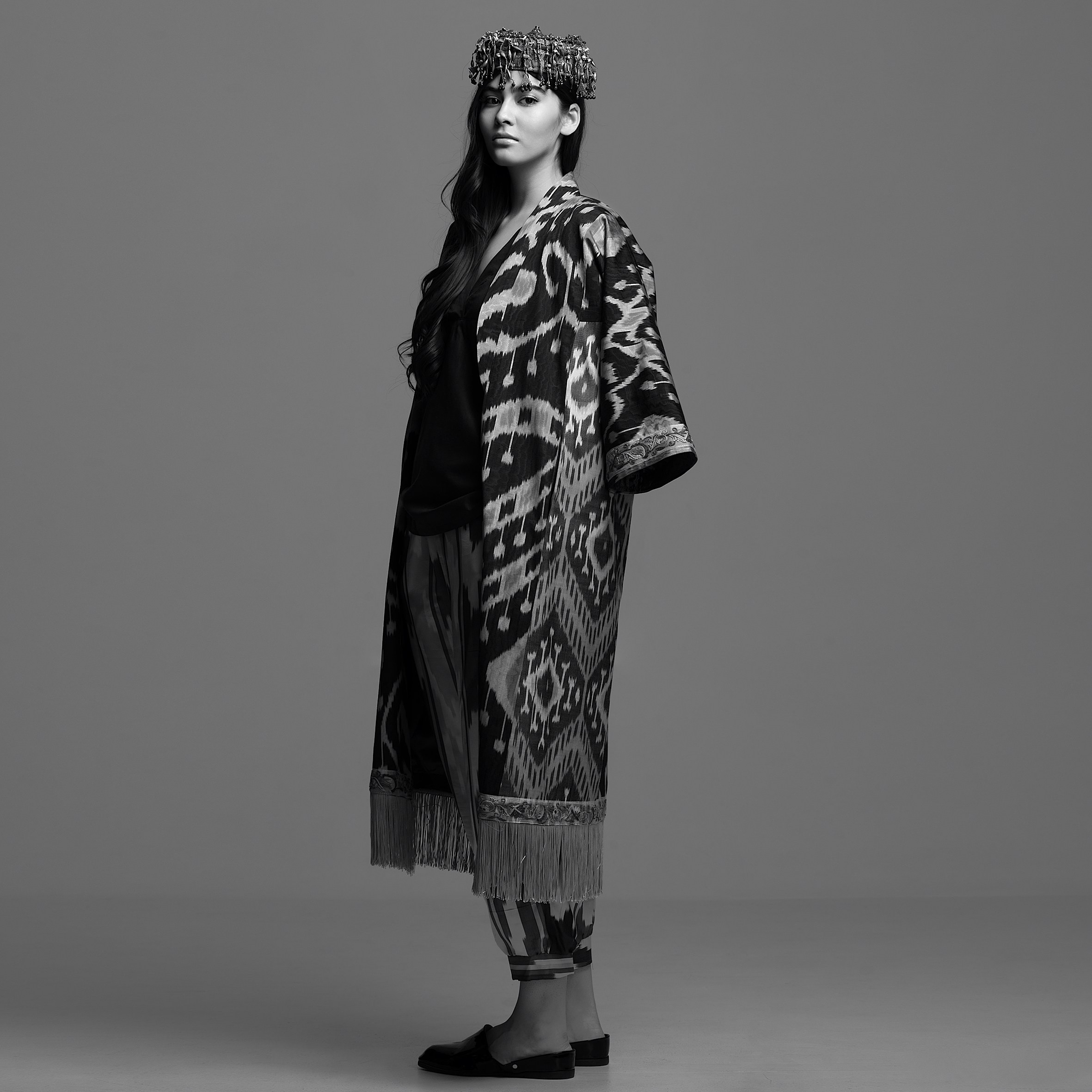 Чёрно-белая fashion-съёмка длинной накидки MURSAK с орнаментальным рисунком, бахромой и головным украшением