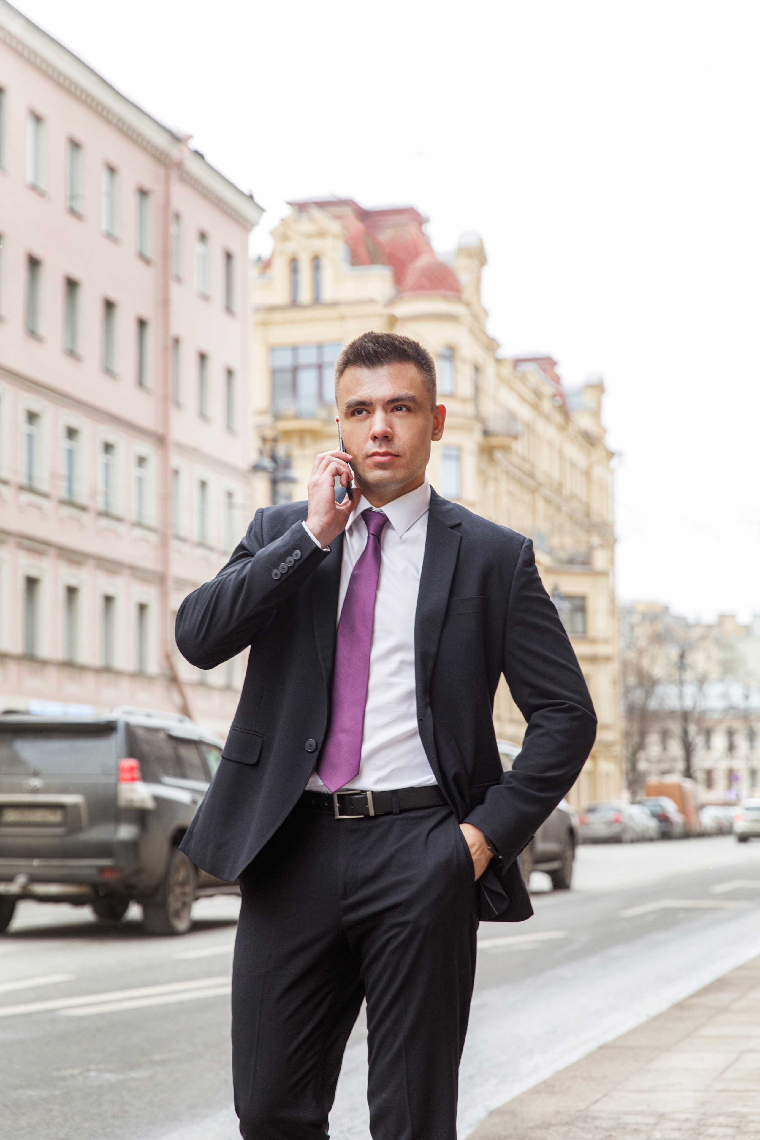 Деловой мужчина в костюме с галстуком идет по улице в СПб и разговаривает по телефону