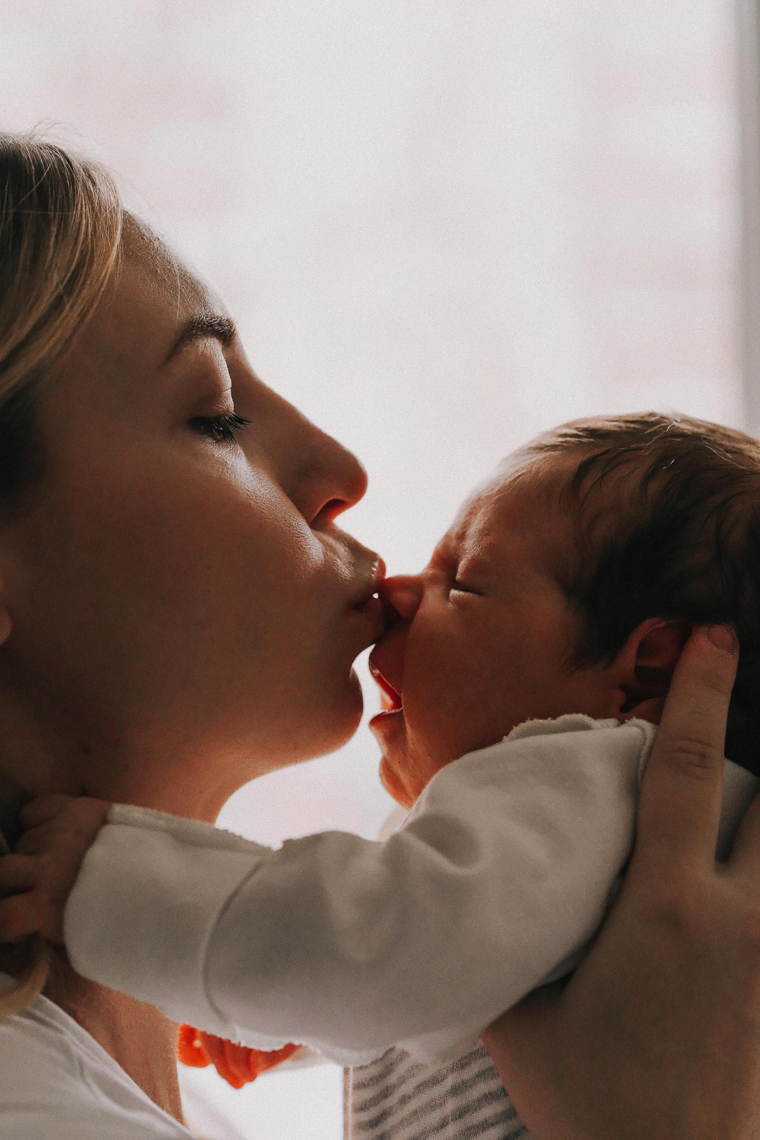 Мама целует своего новорожденного малыша в носик.