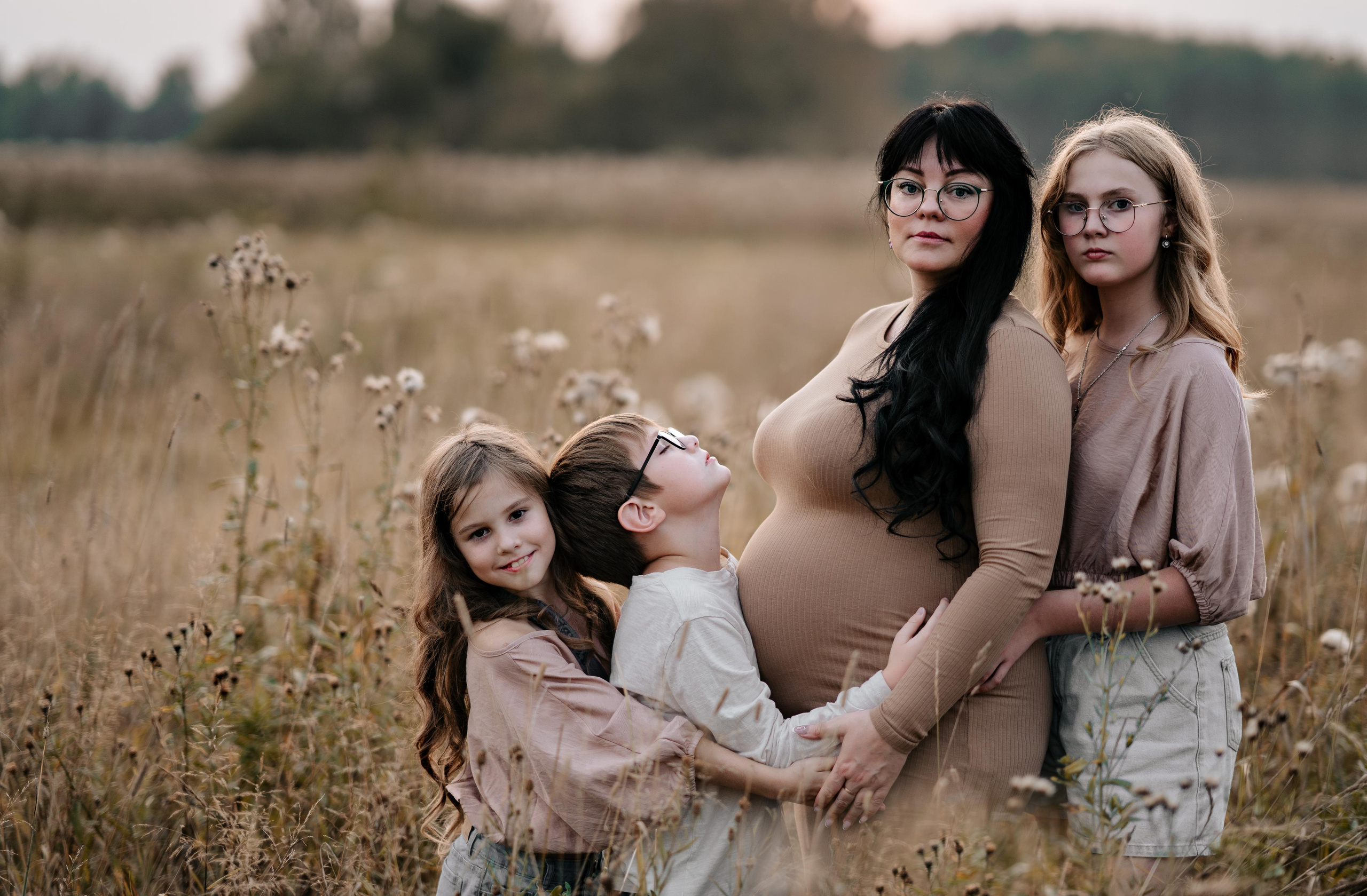 Счастливая беременная мама в окружении старших детей, смотрит в камеру известного фотографа Москвы.