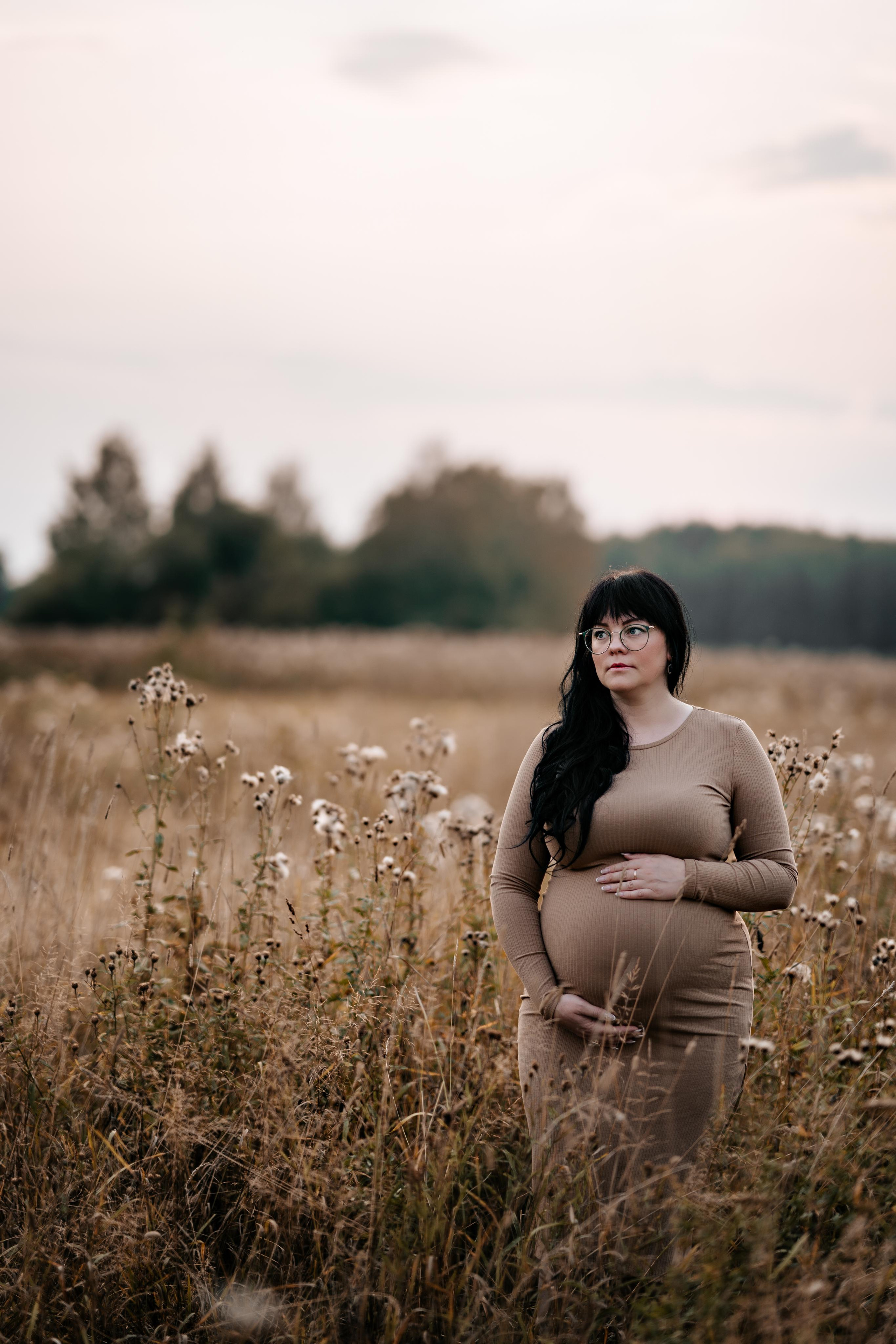 Беременная девушка в поле. Обнимает животик.