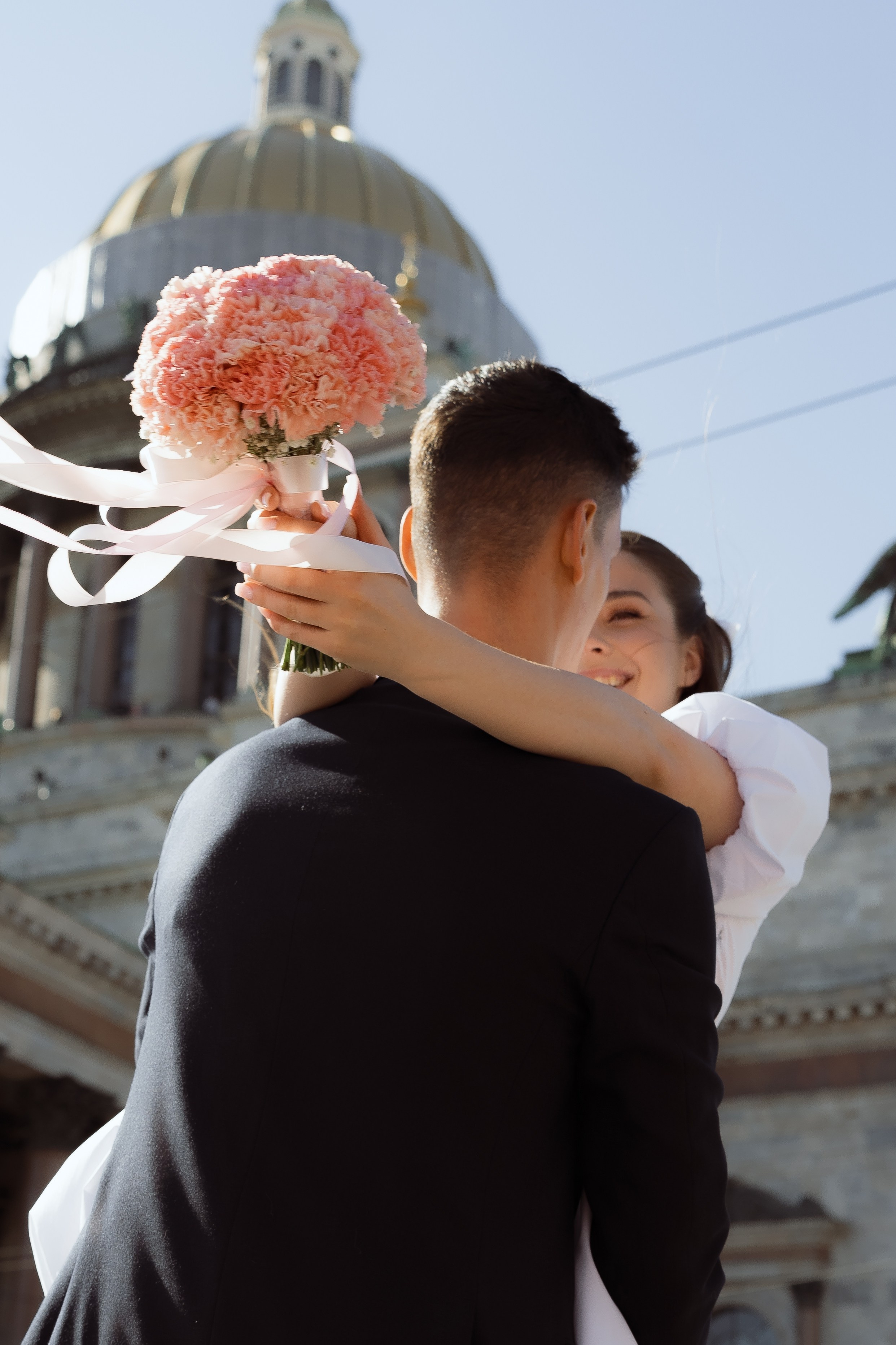 Свадебная пара обнимается с букетом на фоне купола собора