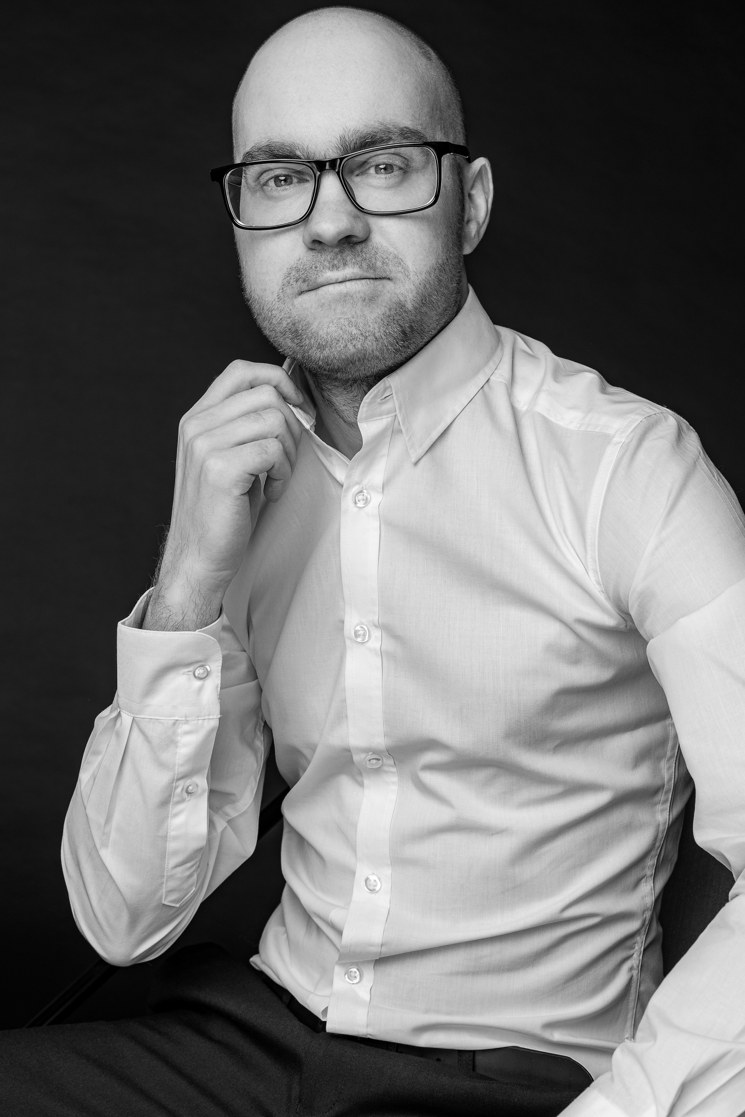 Лысый мужчина в белой рубашке и очках на черном фоне