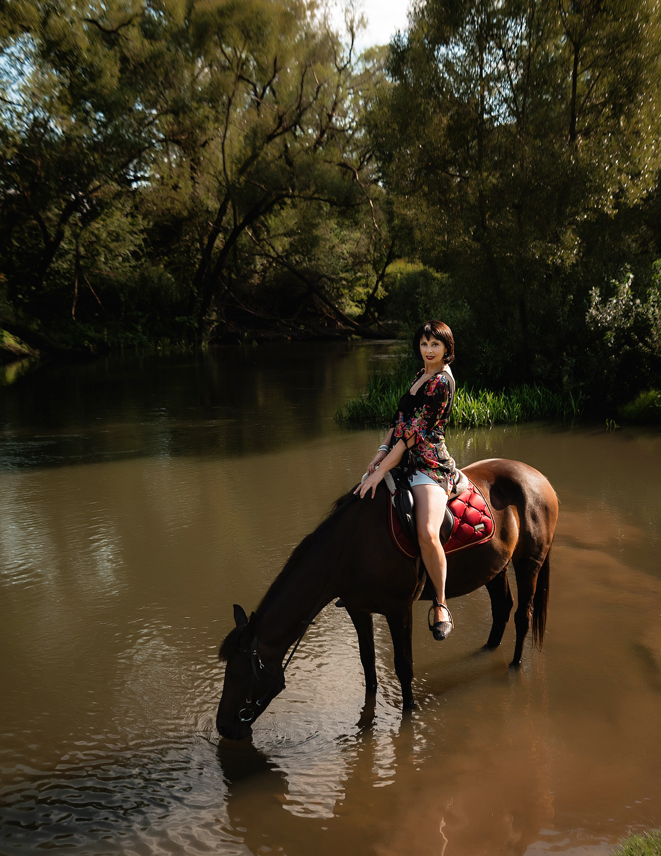 На фото женщина в бежевом платье сидит на лошади, в воде.