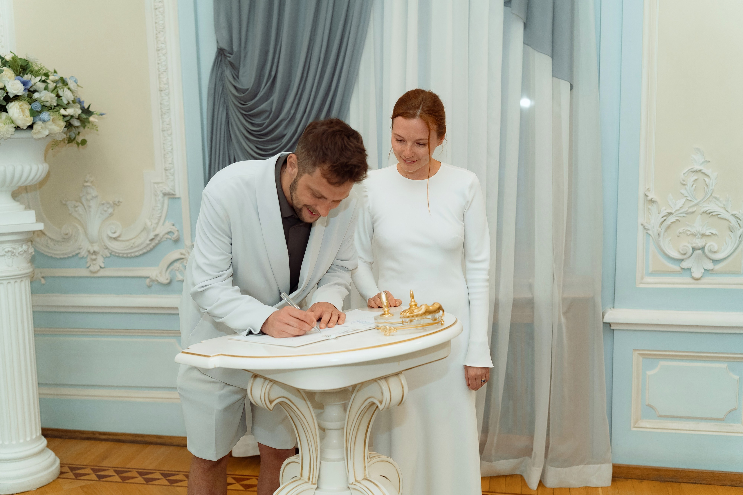 Евгений наклоняется поставить подпись рядом с Марией, белые цветы украшают фон