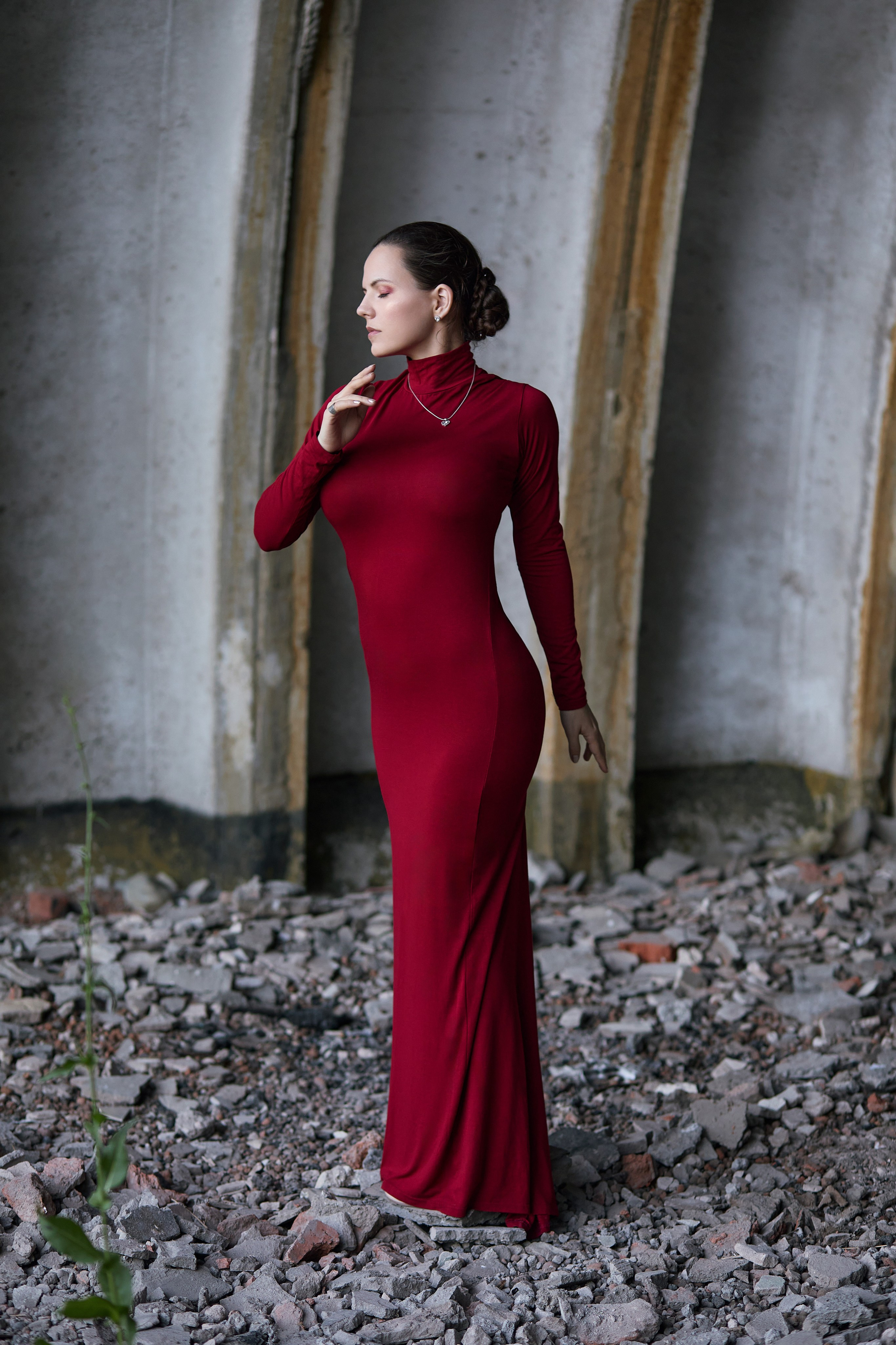 Девушка в длинном красном платье позирует в полный рост внутри старого самолётного ангара