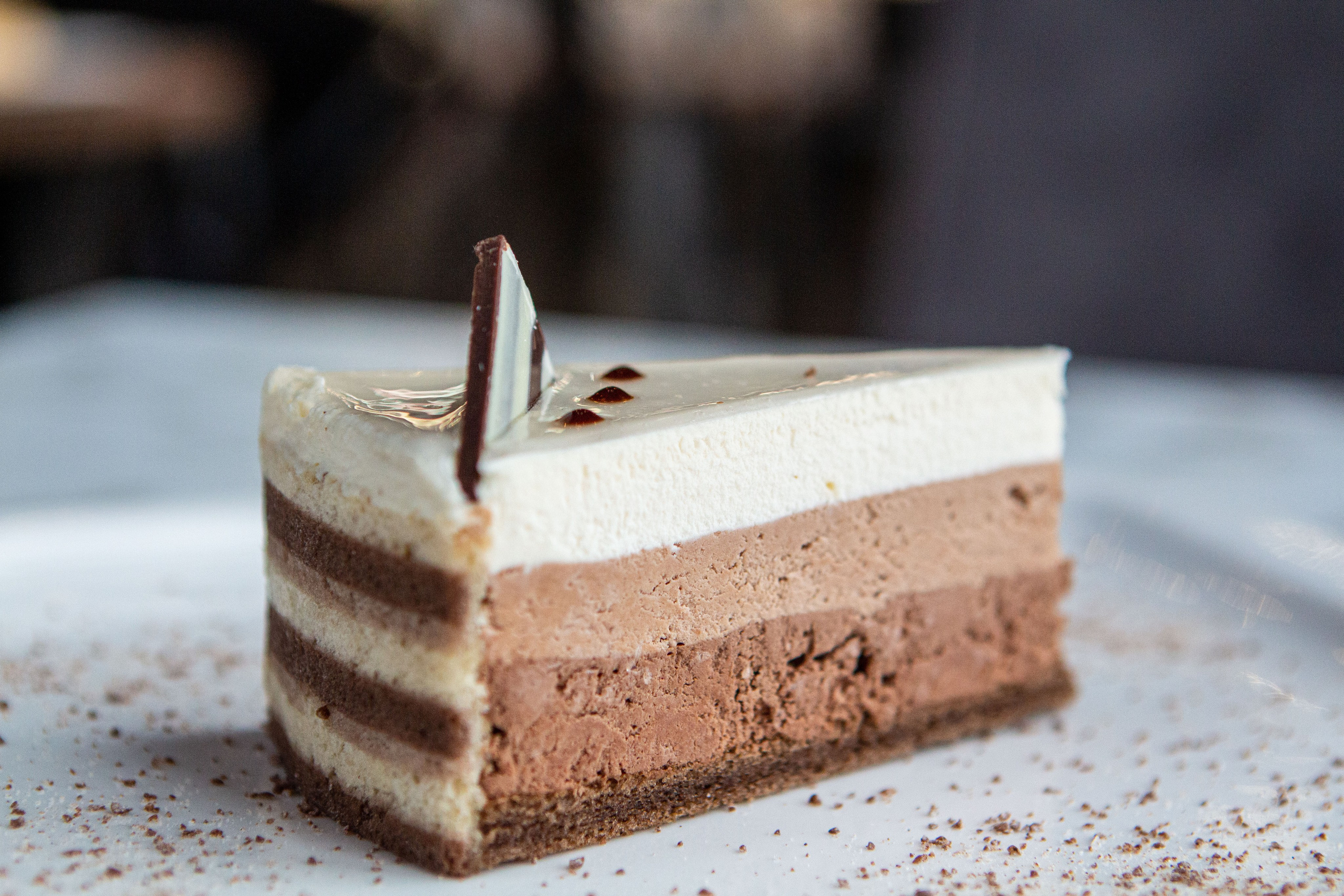 "Торт 'Три шоколада': изысканное сочетание темного, молочного и белого шоколада, украшенное шоколадными крошками и ягодами на белом подносе"