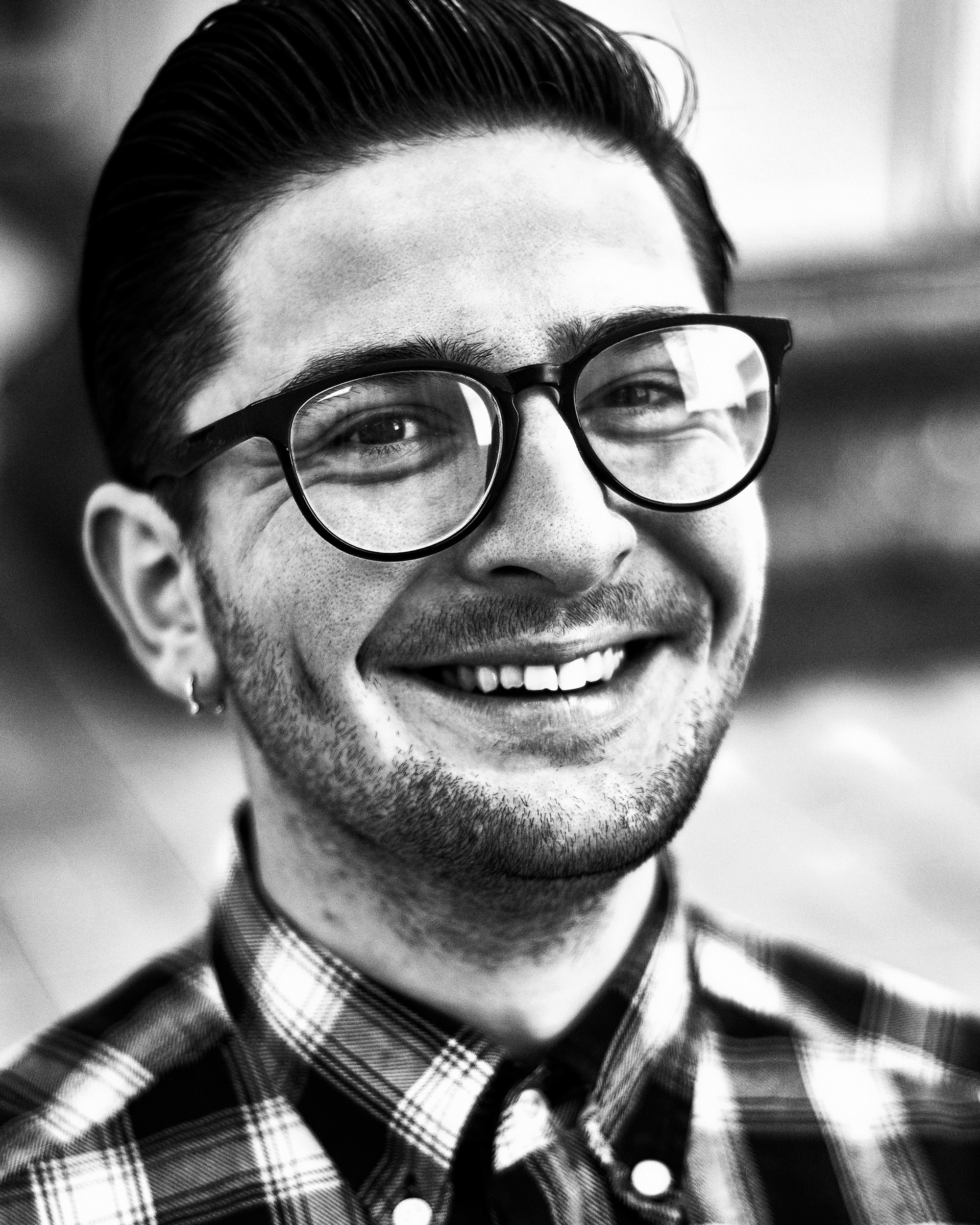 Фотограф Роман Романов — парень улыбается на черно-белом портрете в клетчатой рубашке и очках