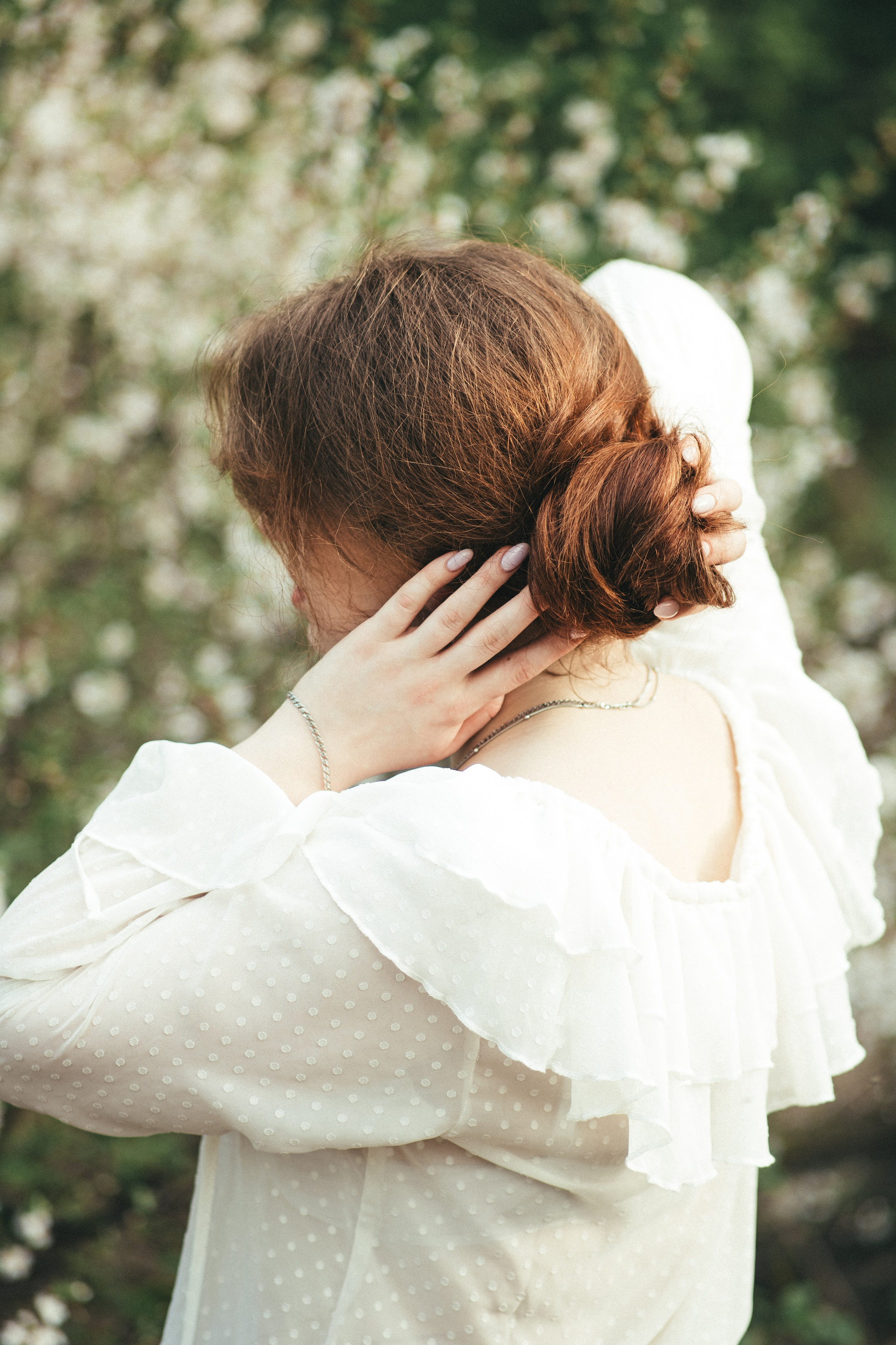 Fine-art фото рыжеволосой девушки в белой блузке со спины волосы в пучок цветущие деревья
